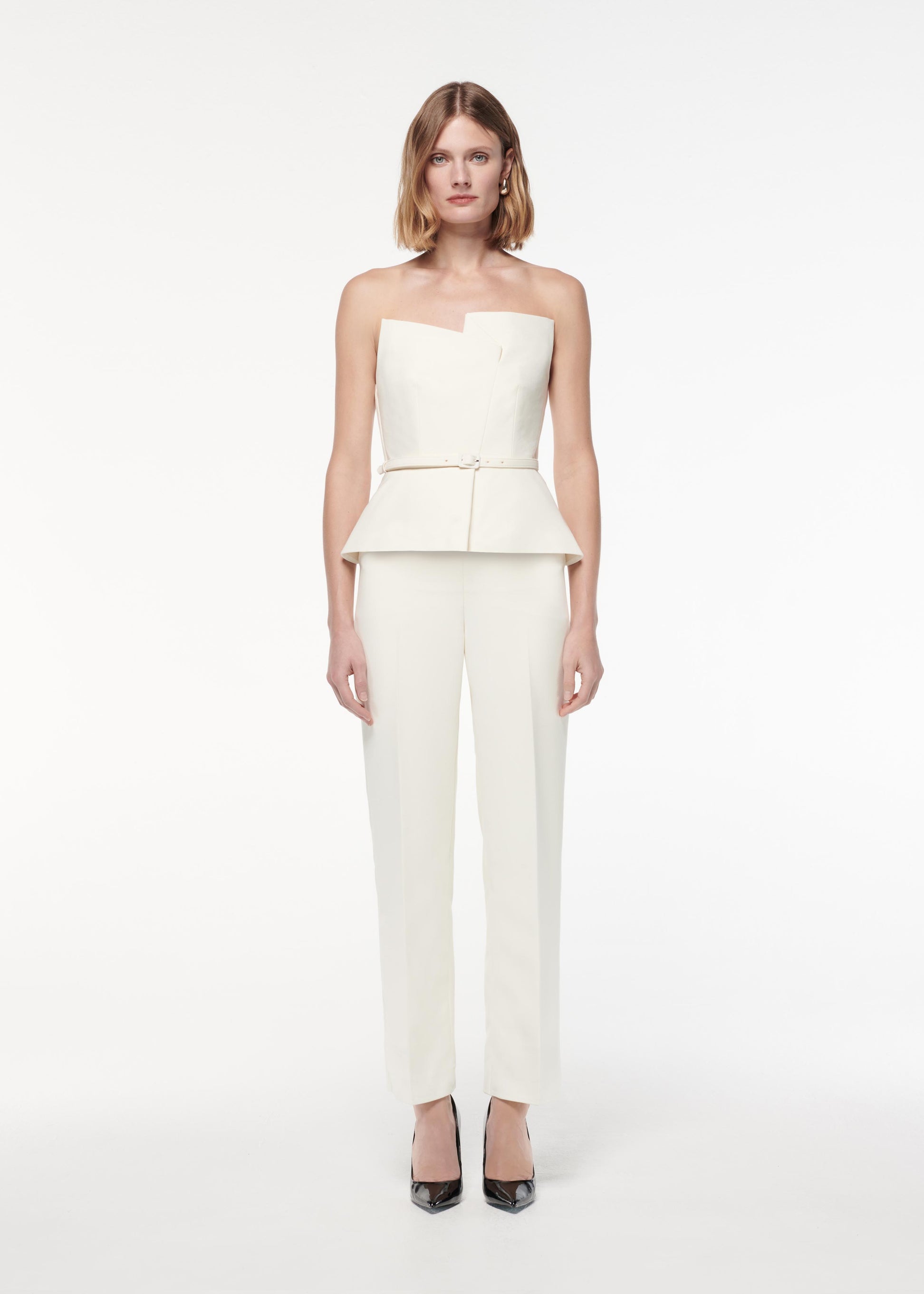 A photograph of a woman wearing a Strapless Peplum Crepe Jumpsuit in Cream
