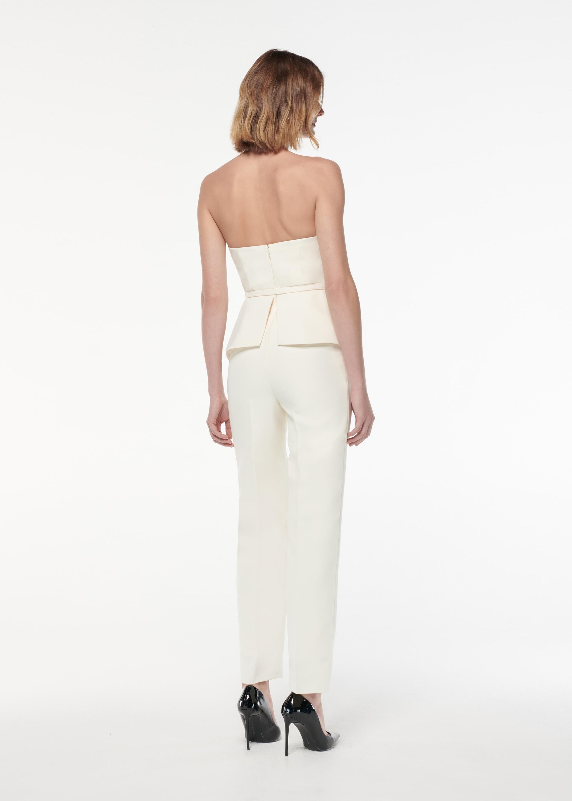 A photograph of a woman wearing a Strapless Peplum Crepe Jumpsuit in Cream