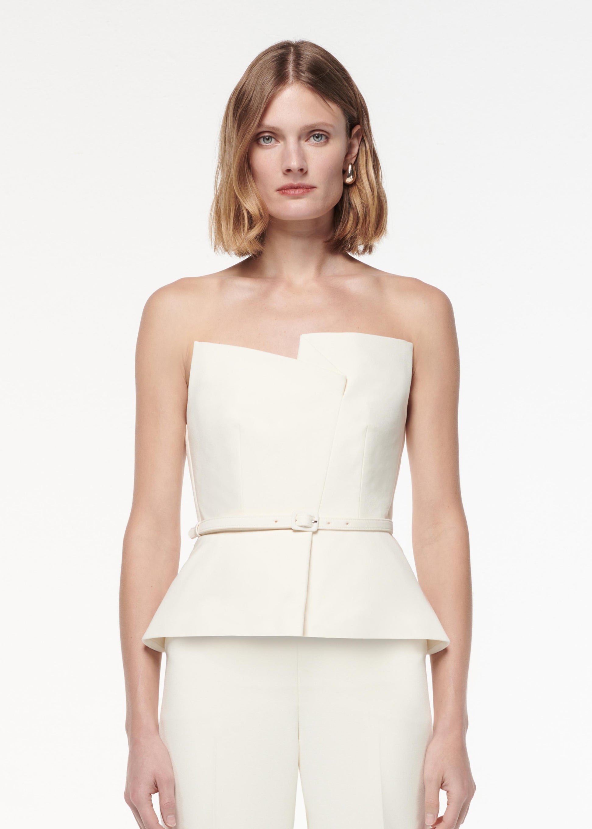 A photograph of a woman wearing a Strapless Peplum Crepe Jumpsuit in Cream