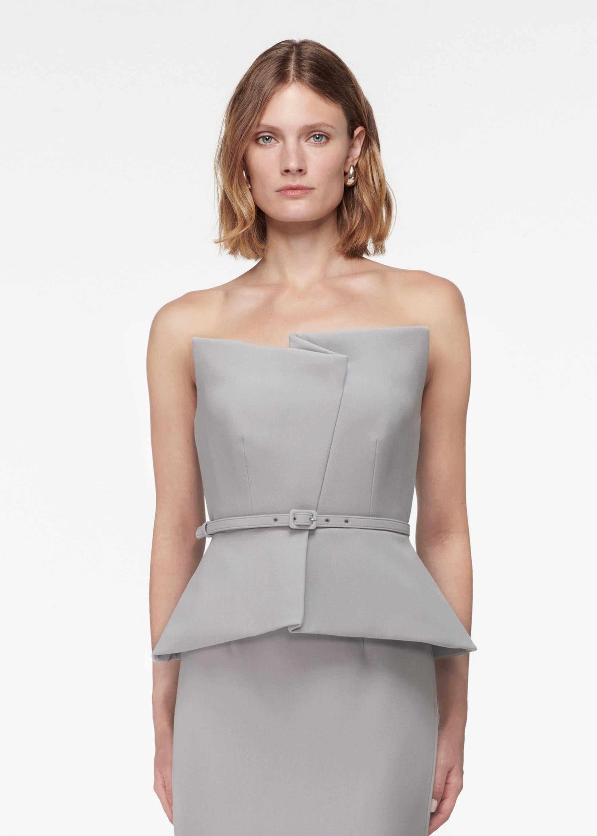 A photograph of a woman wearing a Strapless Crepe Peplum Top in Grey
