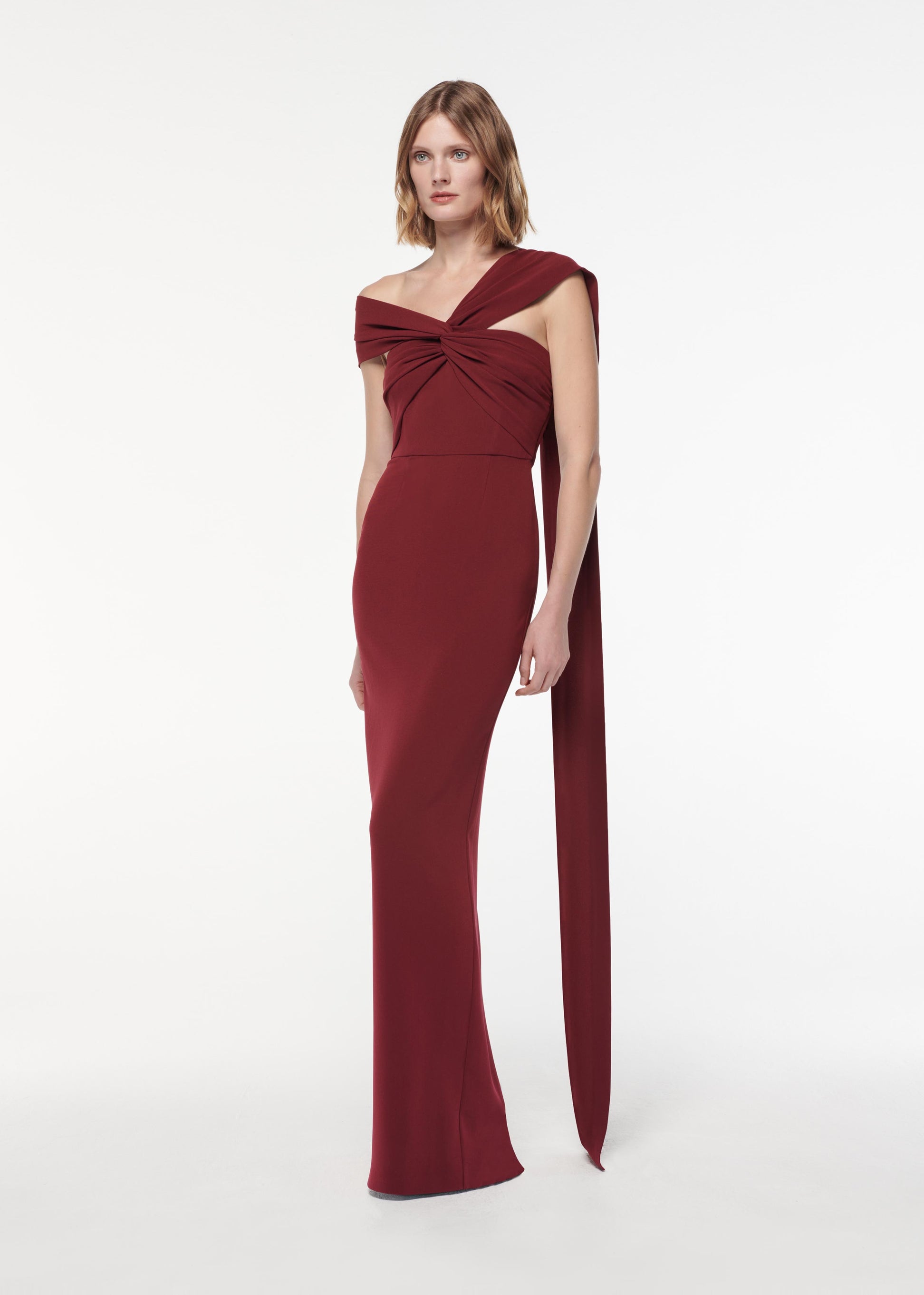 A photograph of a woman wearing a Asymmetric Light Cady Gown in Burgundy