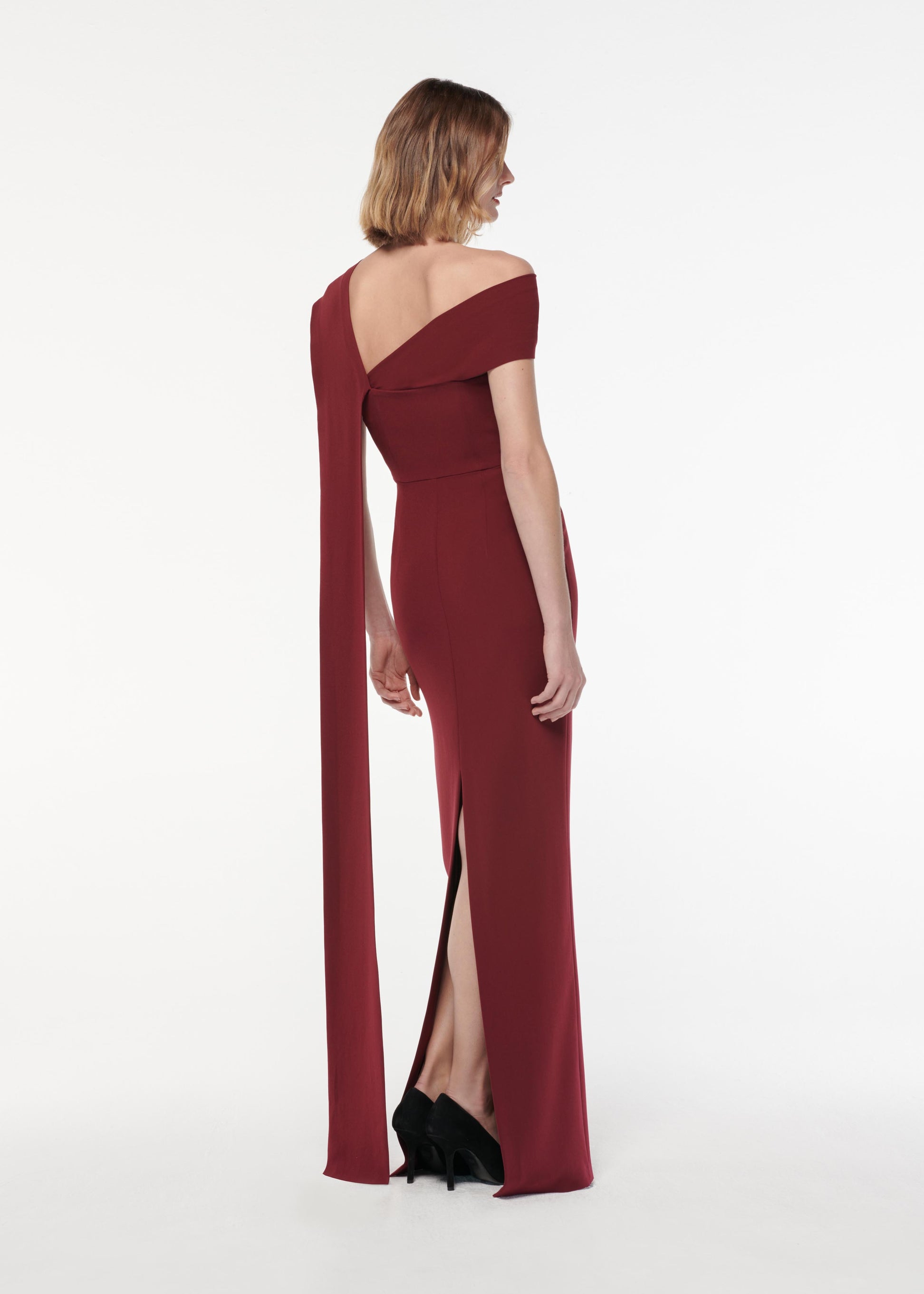 A photograph of a woman wearing a Asymmetric Light Cady Gown in Burgundy