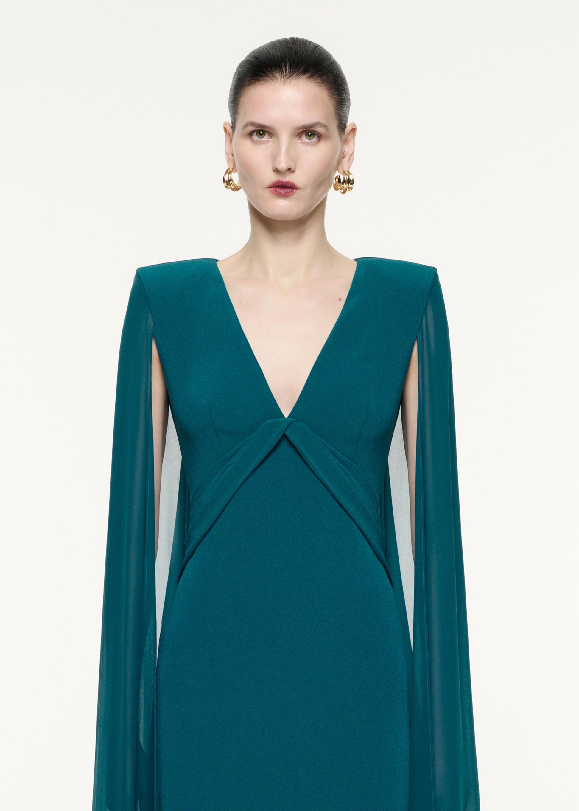 A close up image of a model wearing the Cape Sleeve Satin Crepe Gown in Green