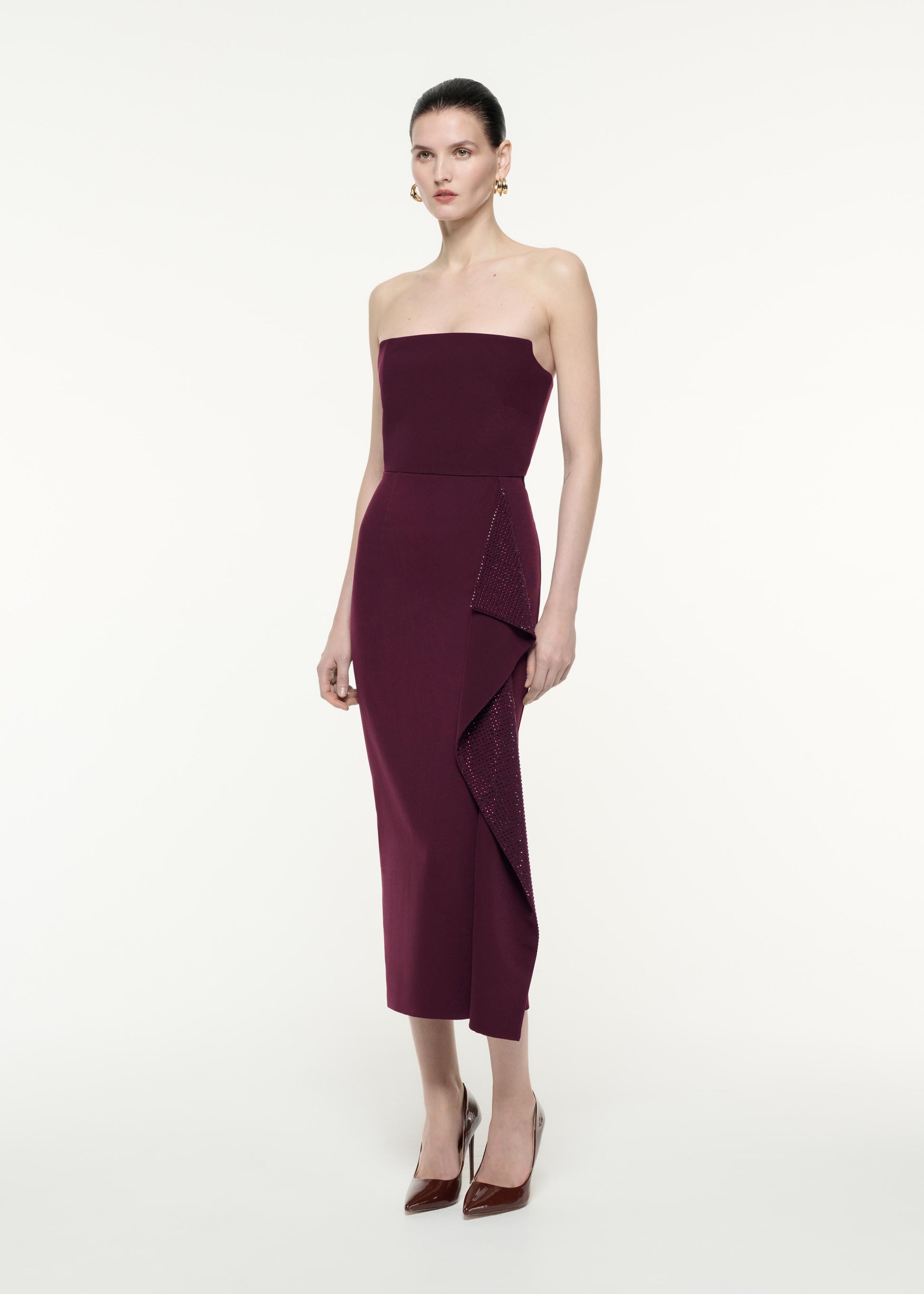 A side view image of a model wearing the Strapless Diamante Ruffle Midi Dress in Aubergine