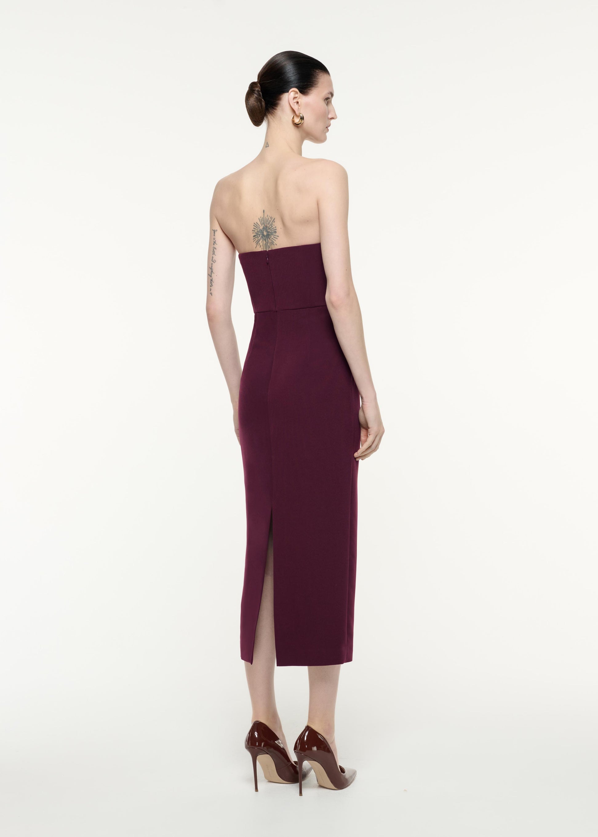A back view image of a model wearing the Strapless Diamante Ruffle Midi Dress in Aubergine