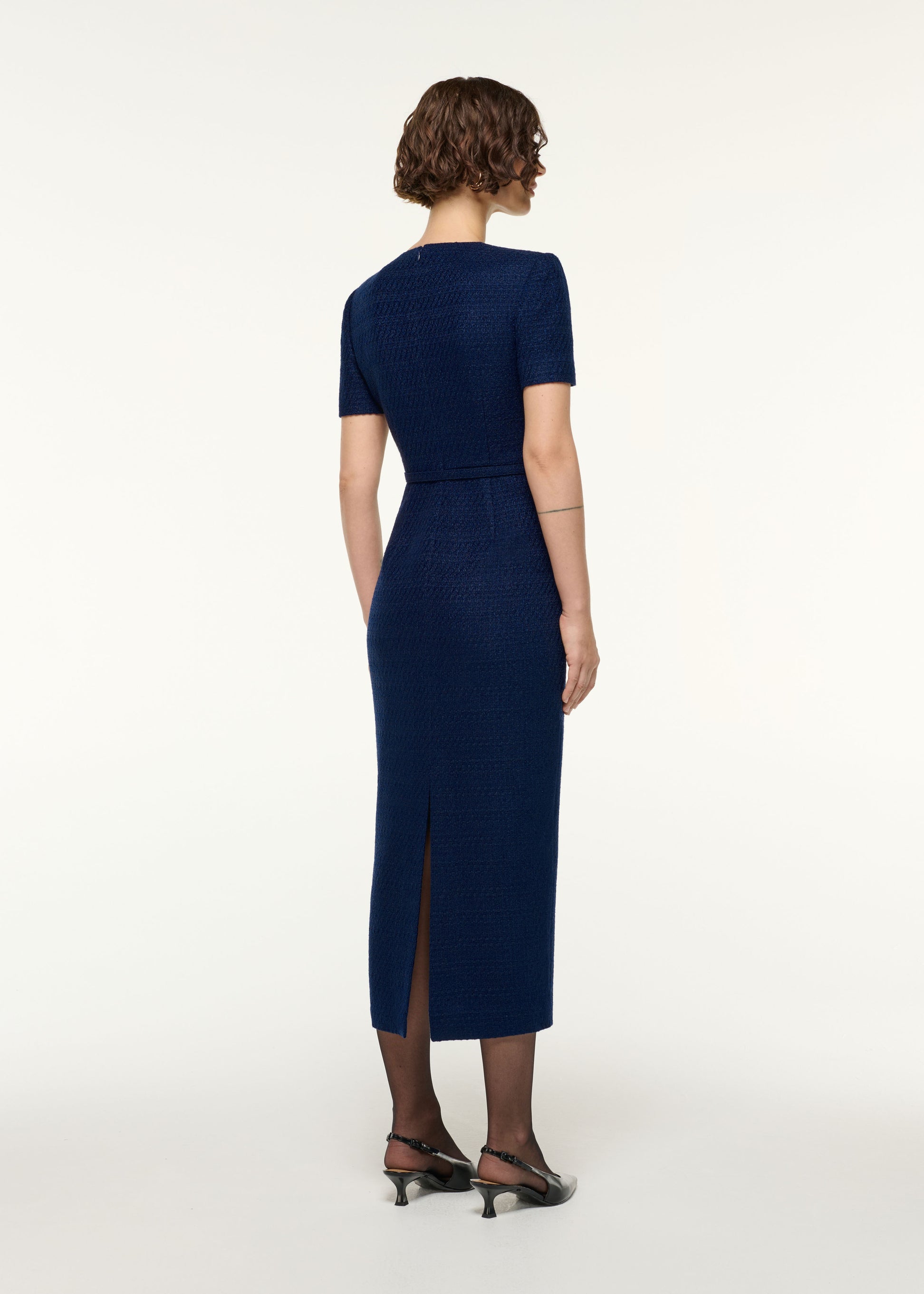 Back view of a model wearing the Twisted Silver Brooch Belted Boucle Dress in Navy