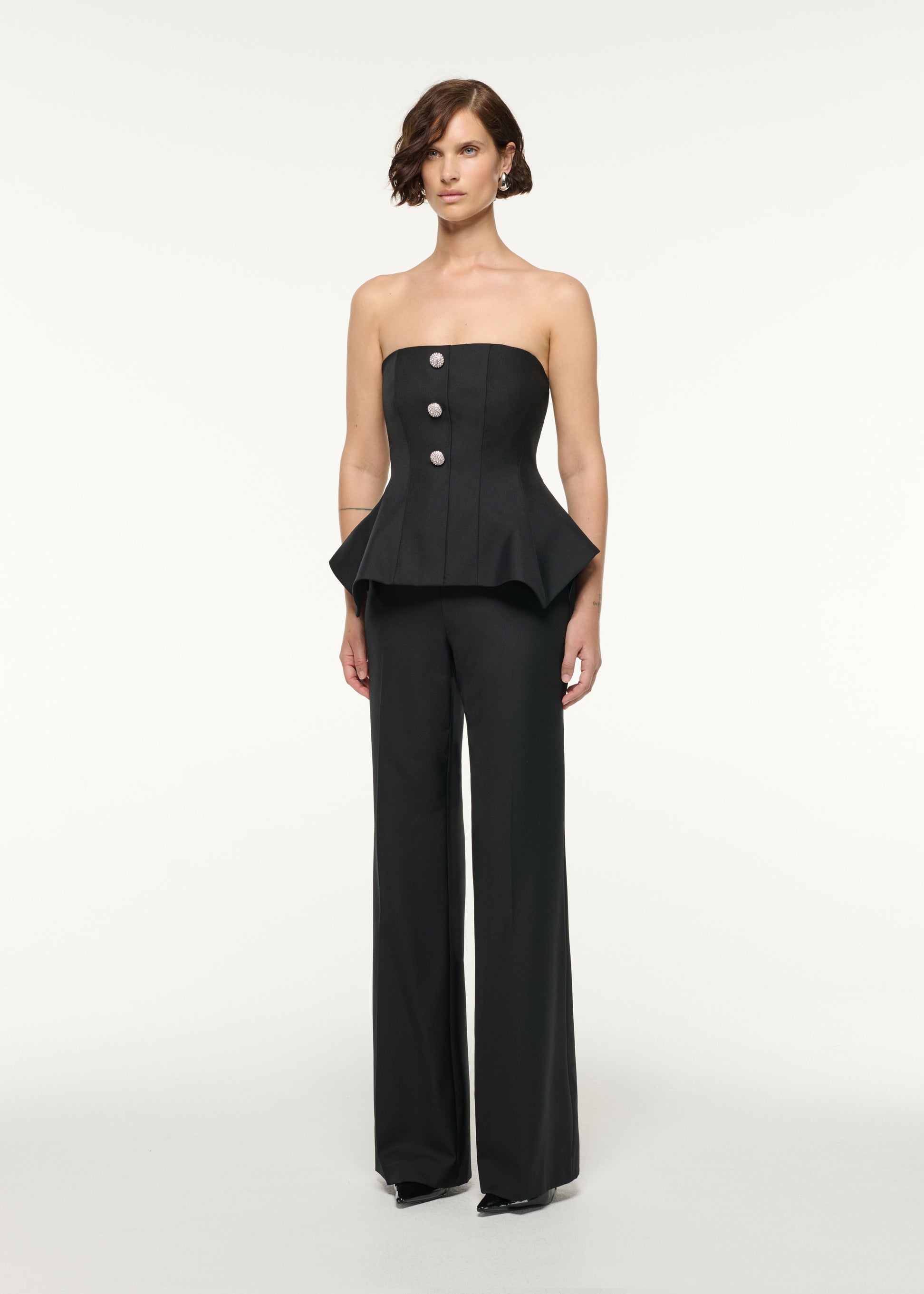 Side view of a model wearing the Crystal Button Peplum Wool Jumpsuit in Black