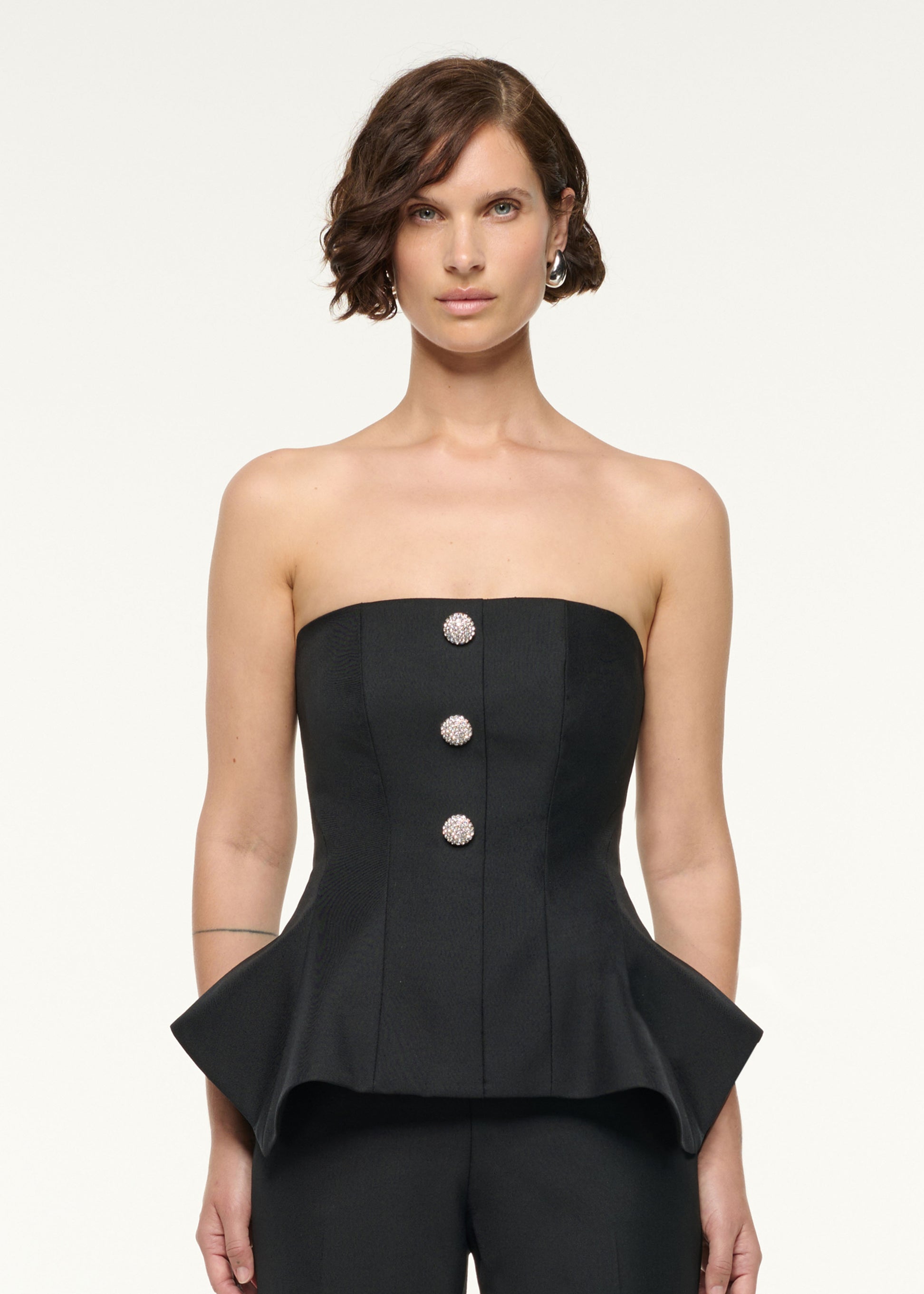 Close up of a model wearing the Crystal Button Peplum Wool Jumpsuit in Black