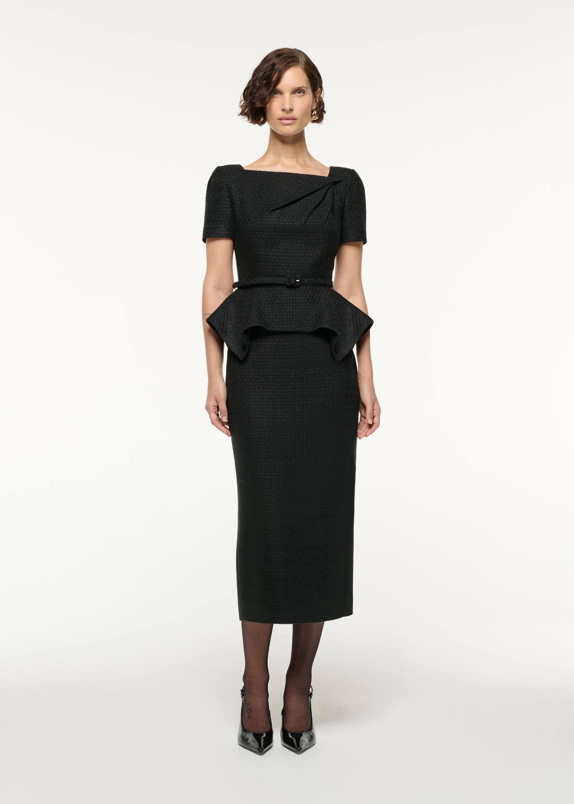 Front view of a model wearing the Asymmetrical Twist Peplum Boucle Dress in Black