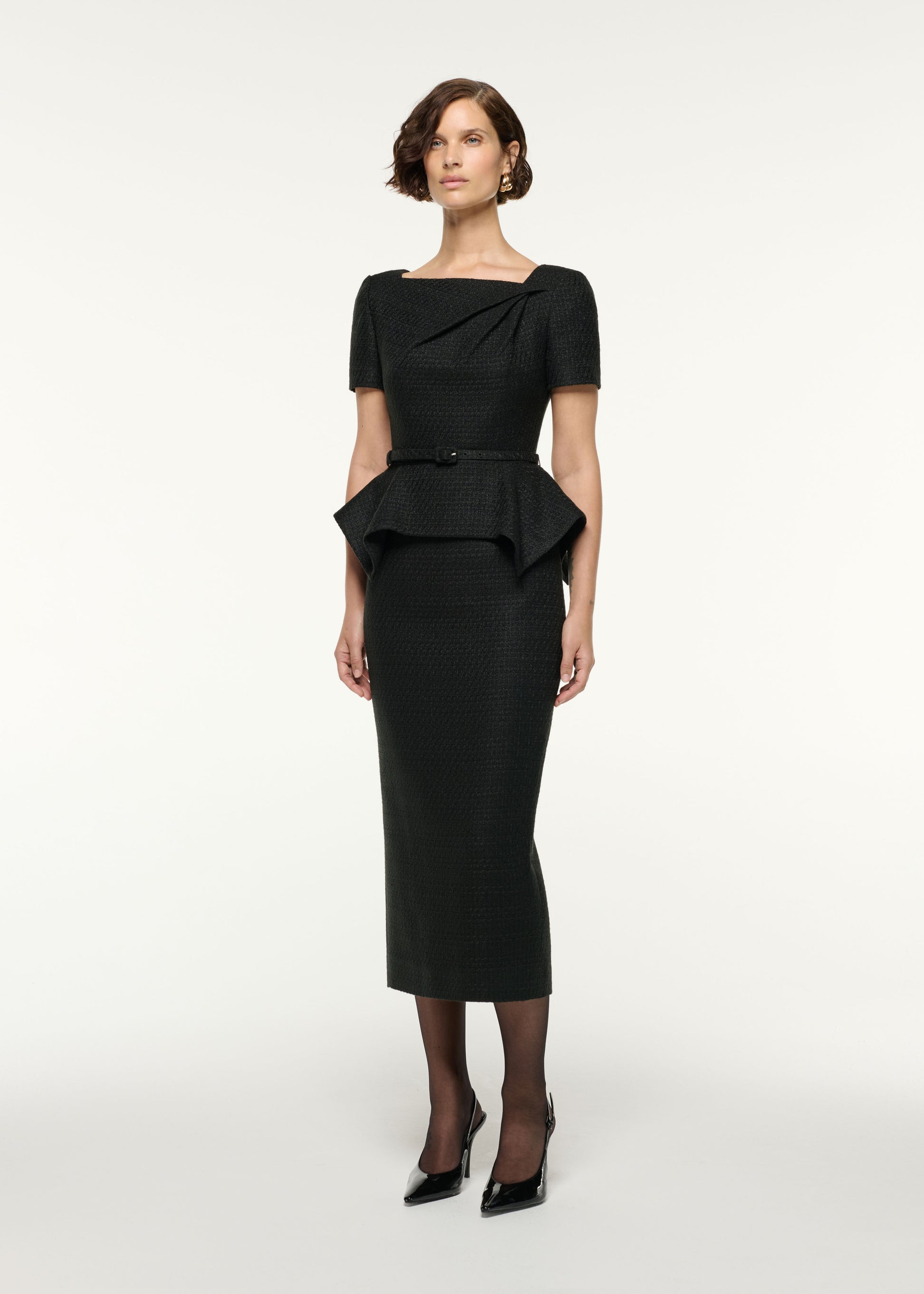 Side view of a model wearing the Asymmetrical Twist Peplum Boucle Dress in Black