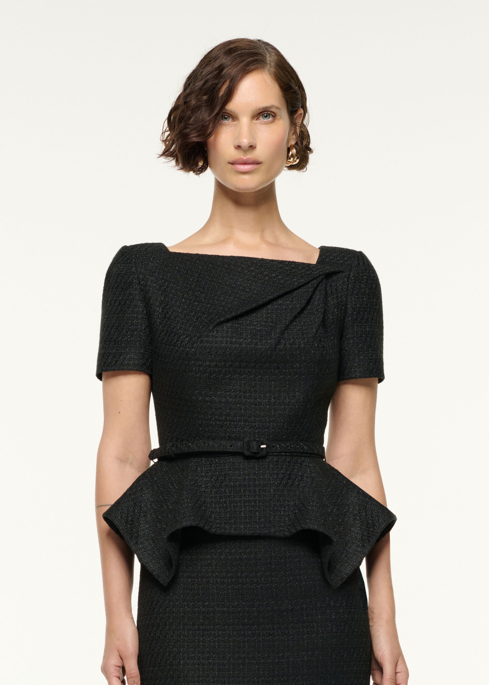 Close up of a model wearing the Asymmetrical Twist Peplum Boucle Dress in Black