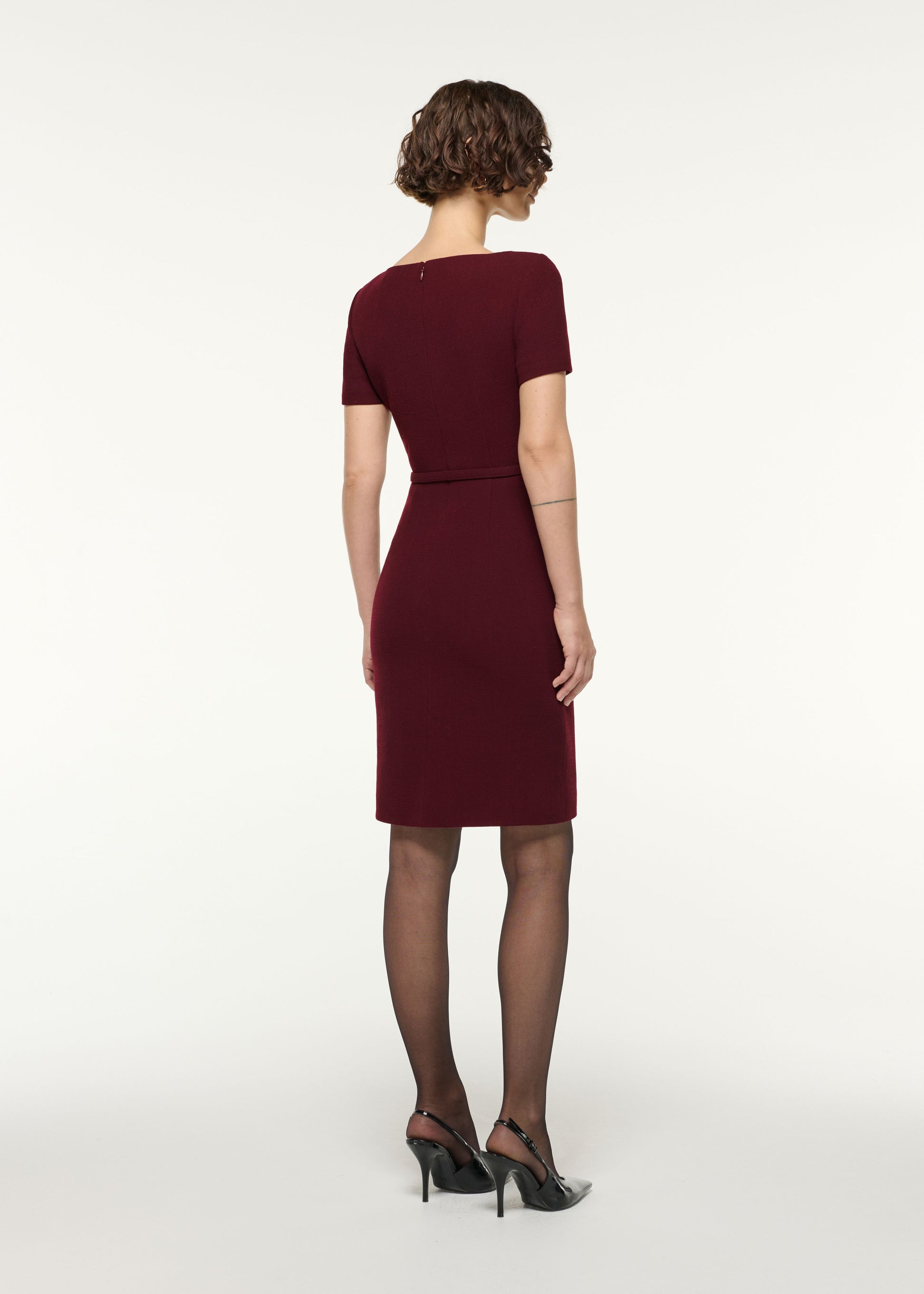 Back view of a model wearing the Asymmetrical Twist Belted Wool Dress in Mulberry