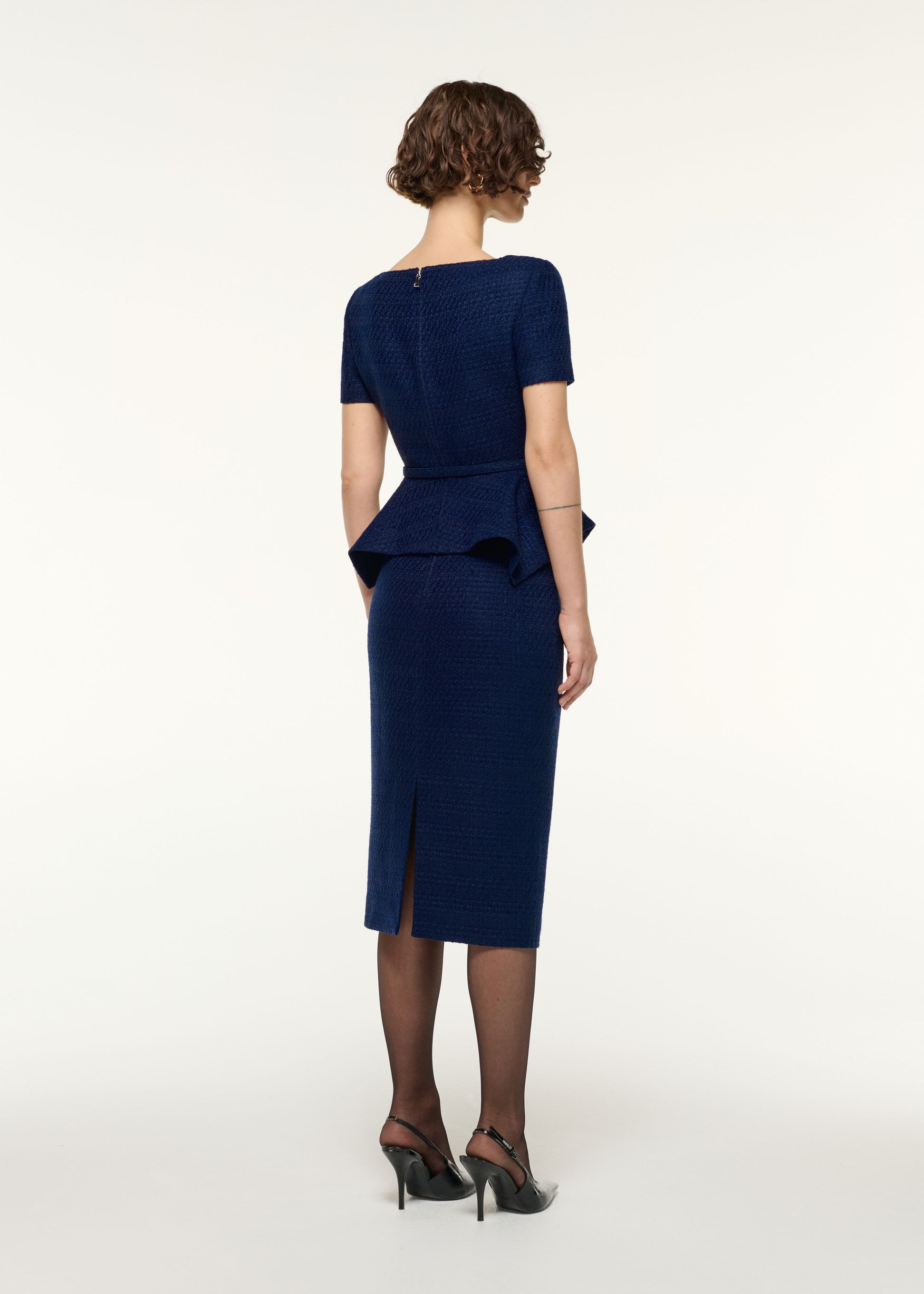 Back view of a model wearing the Asymmetrical Twist Peplum Boucle Top in Navy