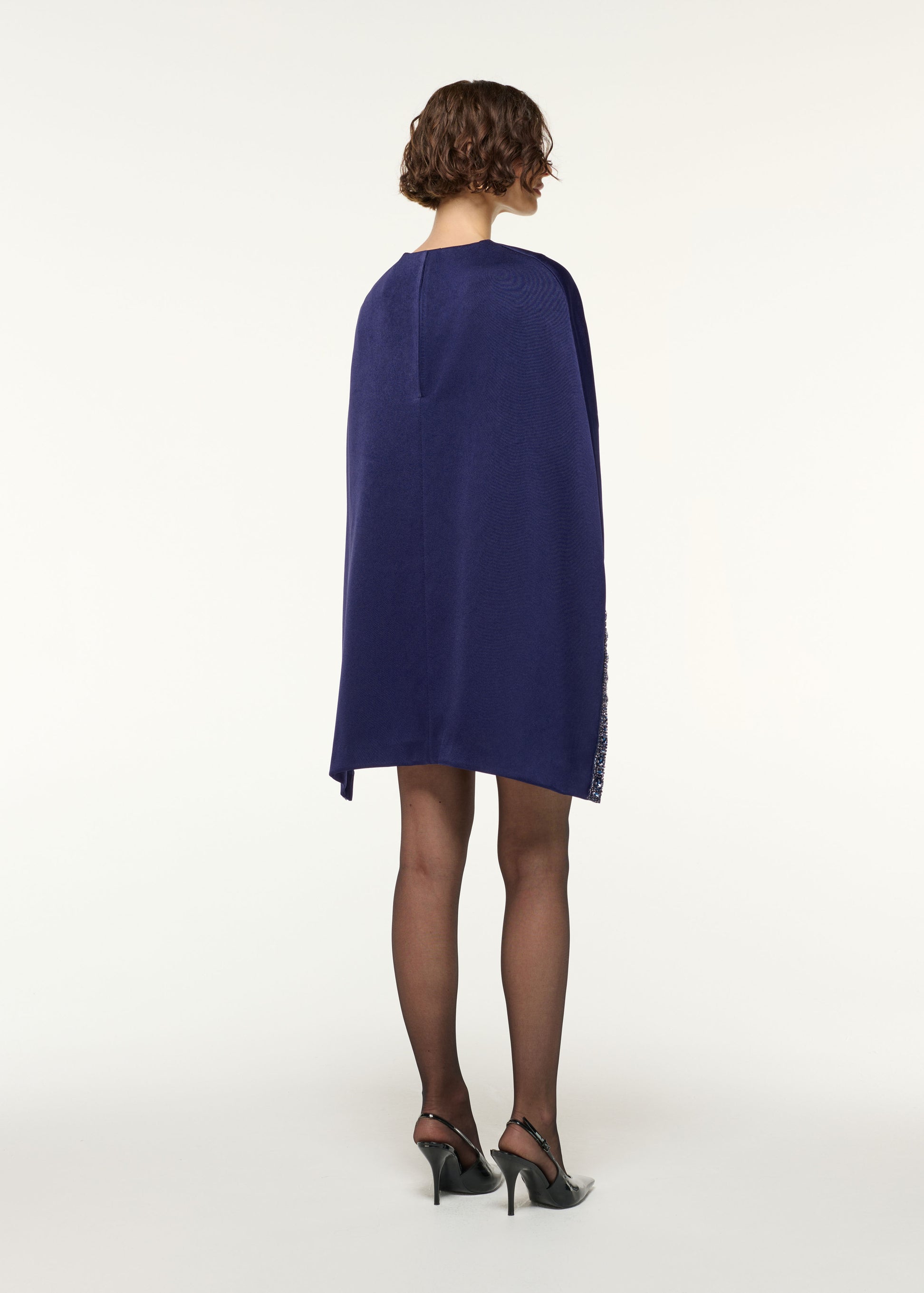 Back view of a model wearing the Crystal Trimmed Cape Mini Dress in Navy