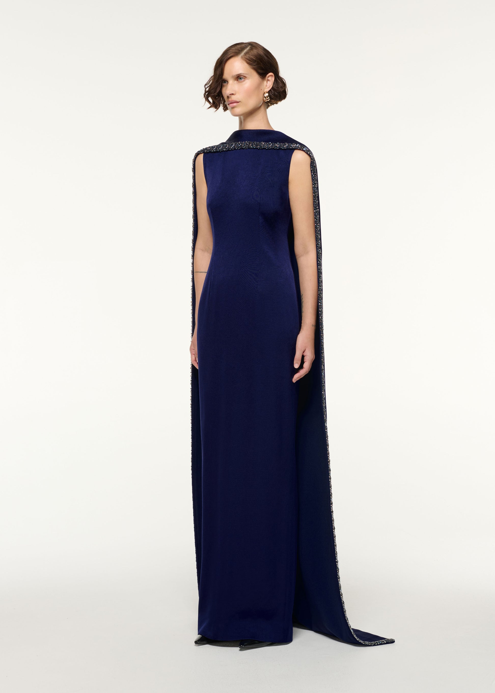 Side view of a model wearing the Crystal Trimmed Cape Gown in Navy