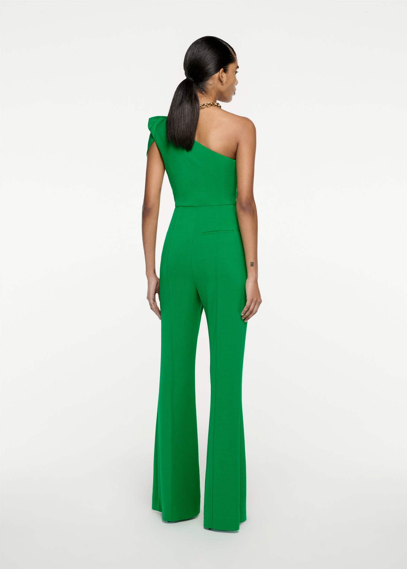 The back of a woman wearing the Asymmetric Stretch Cady Jumpsuit in Green