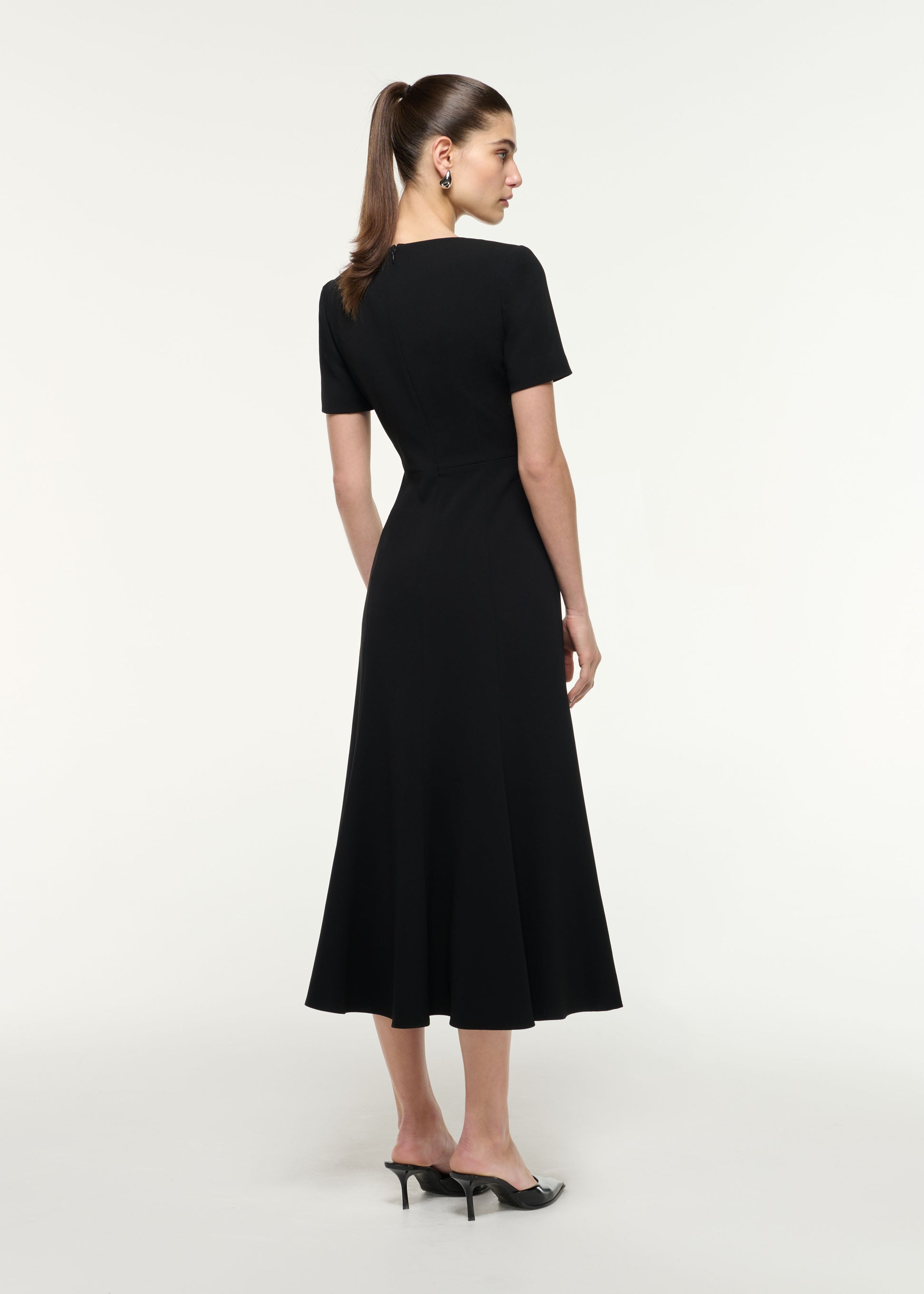 Back view of a model wearing the Shoulder Drape Midi Dress in Black