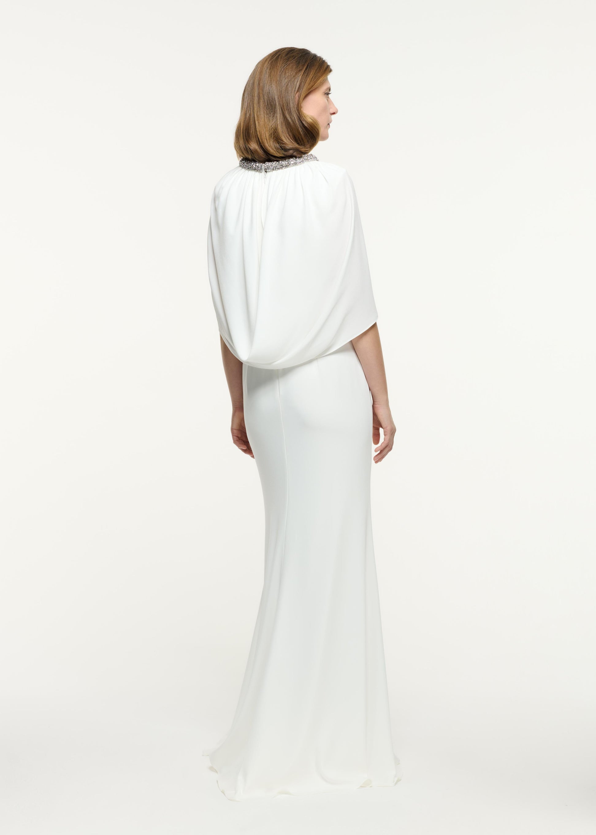 Back view of a model wearing the Embellished Cape Satin Crepe Gown in White