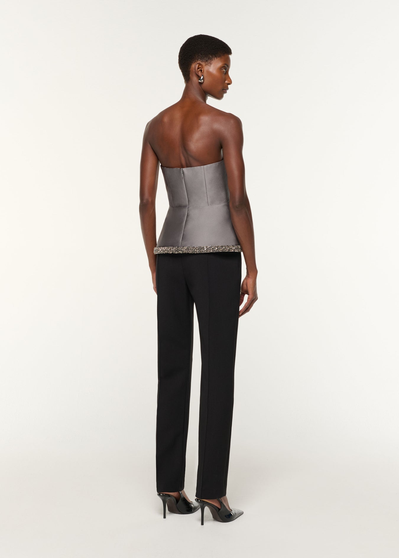 Back view of a model wearing the Square Neck With Crystal Trim Peplum Taffeta Top in Grey