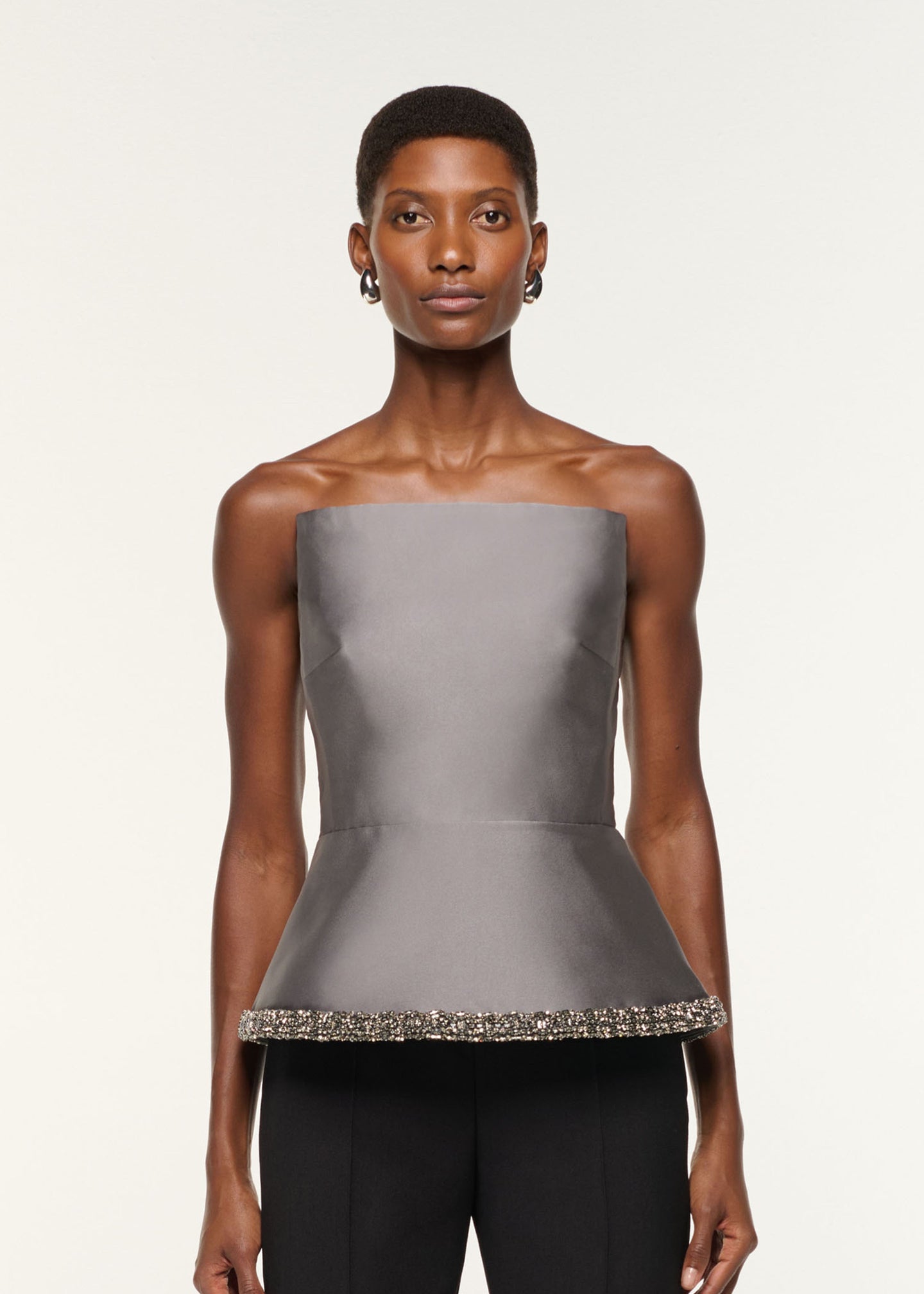 Close up of a model wearing the Square Neck With Crystal Trim Peplum Taffeta Top in Grey