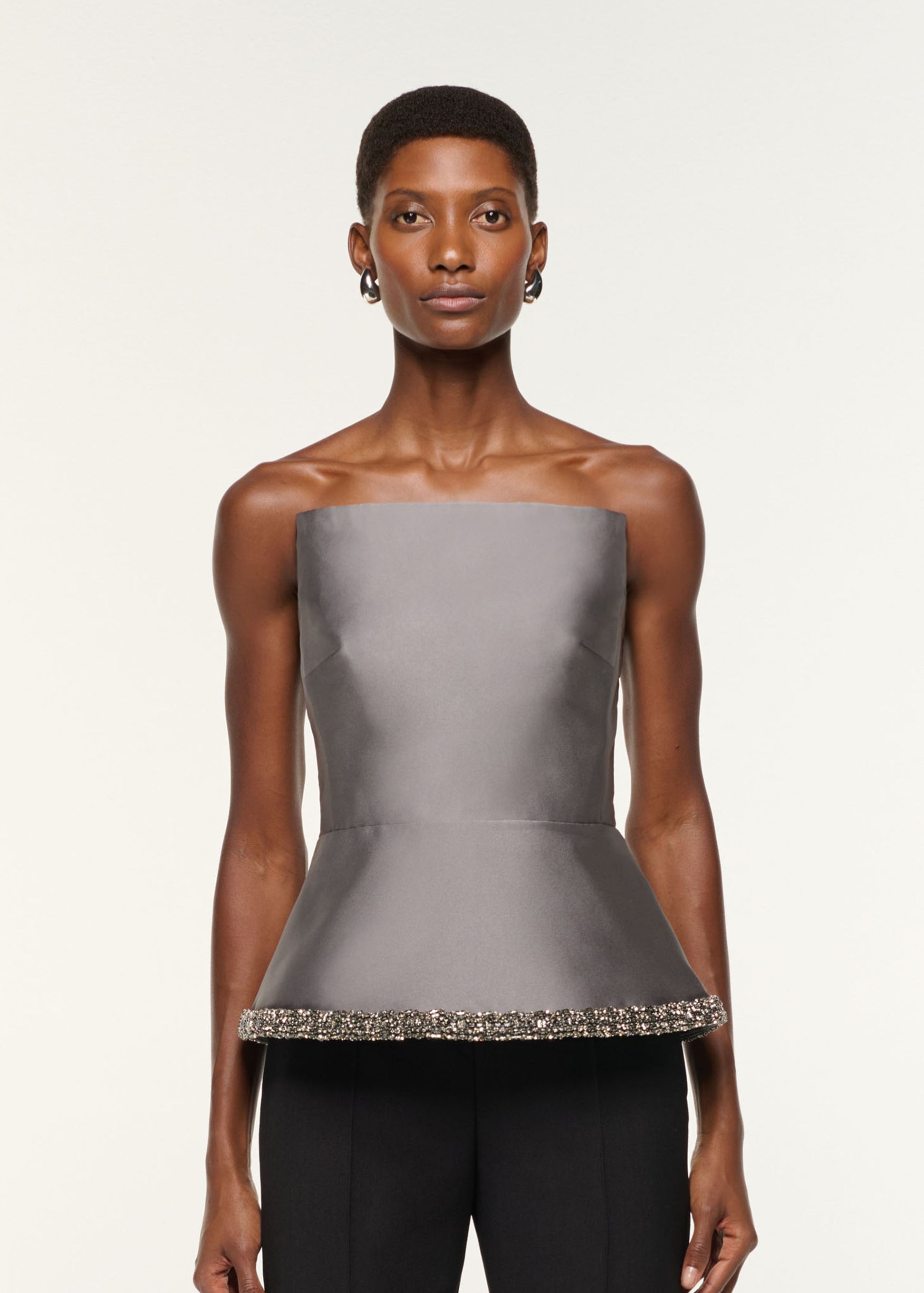 Close up of a model wearing the Square Neck With Crystal Trim Peplum Taffeta Top in Grey