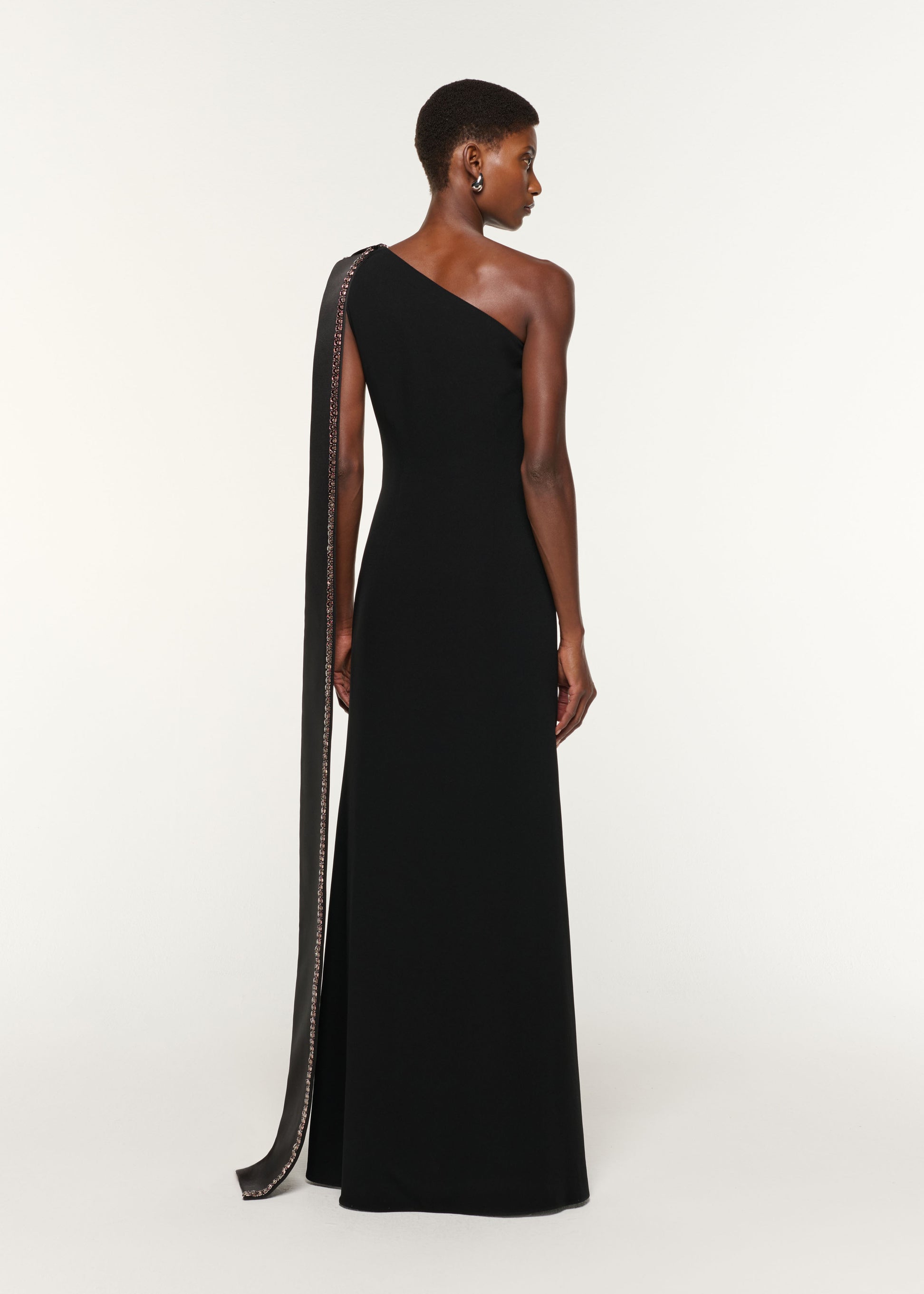 Back view of a model wearing the Contrast Crystal Trimmed Bow Satin Crepe Gown in Black