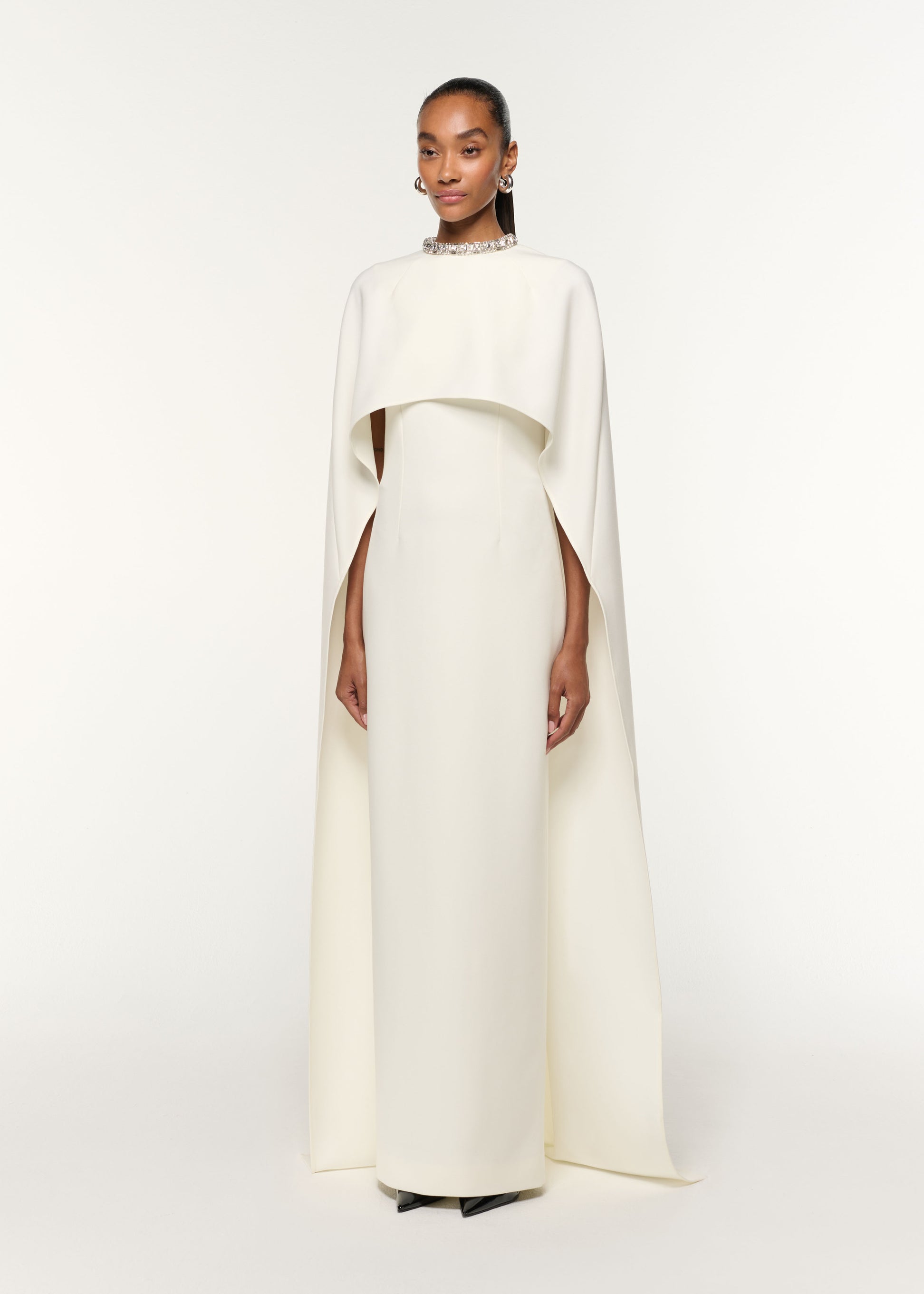 Side view of a model wearing the Crystal Neckline Crepe Cape Gown in Cream