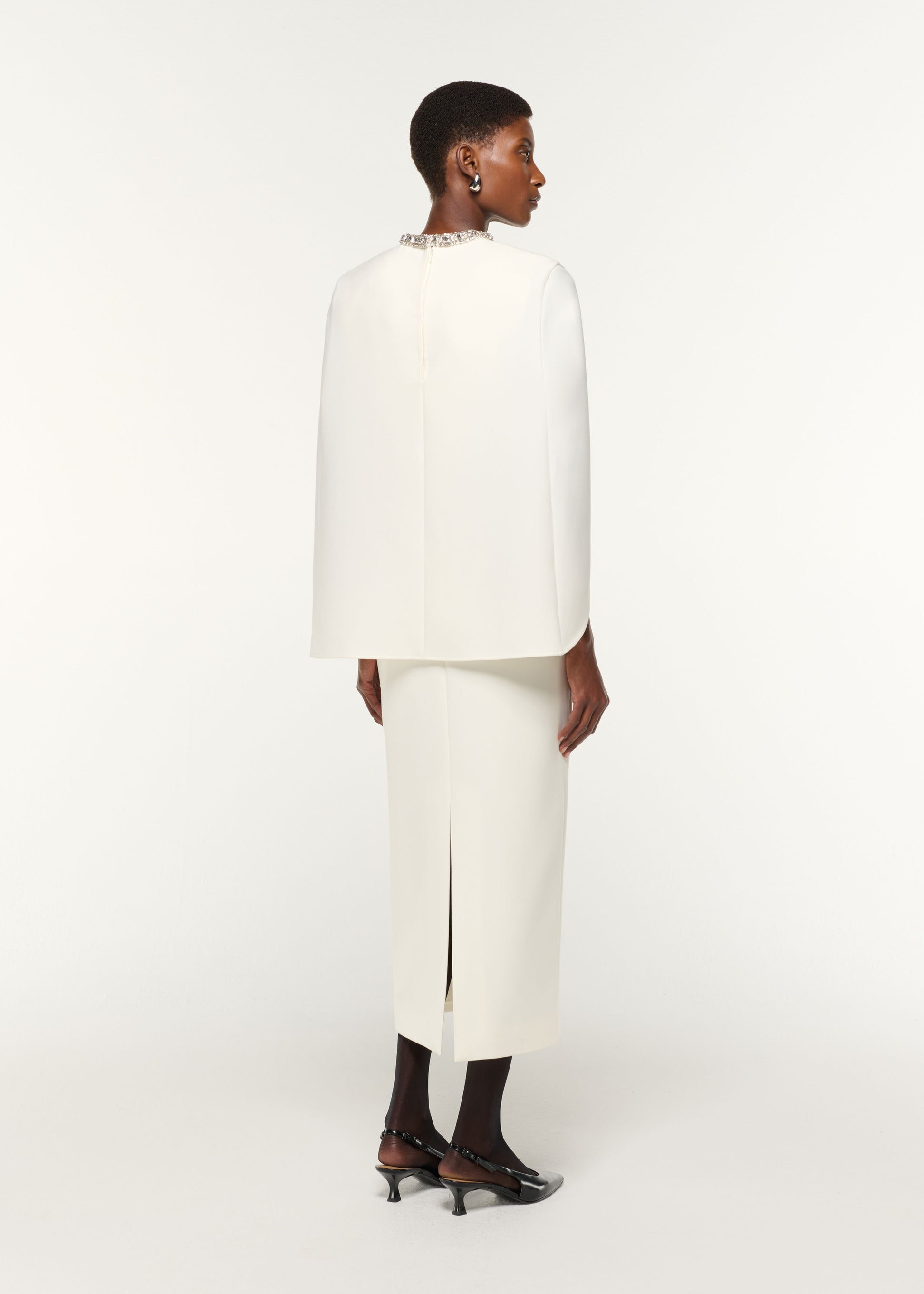 Back view of a model wearing the Crystal Neckline Crepe Cape Dress in Cream