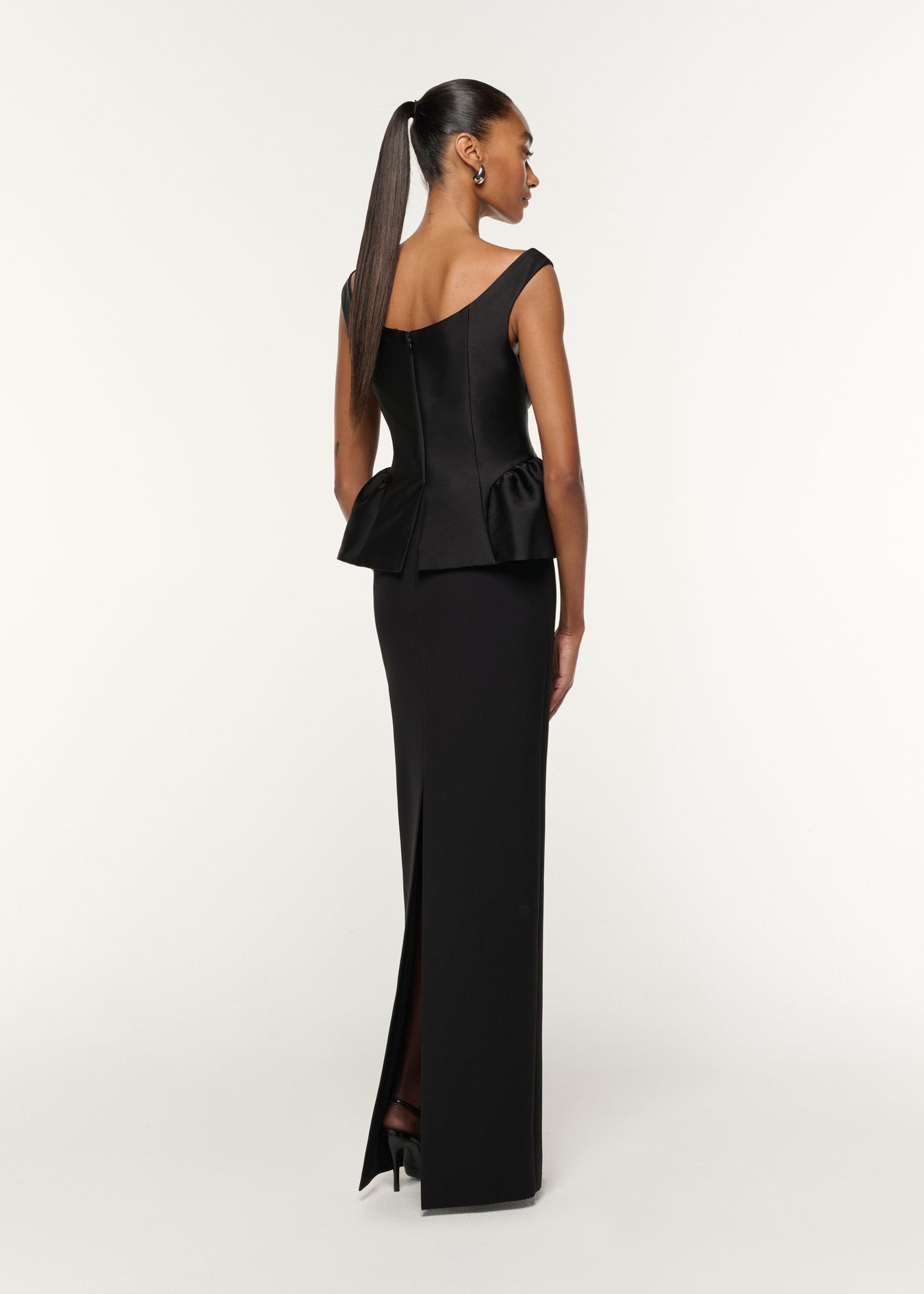 Back view of a model wearing the Crystal Button Peplum Taffeta Crepe Gown in Black