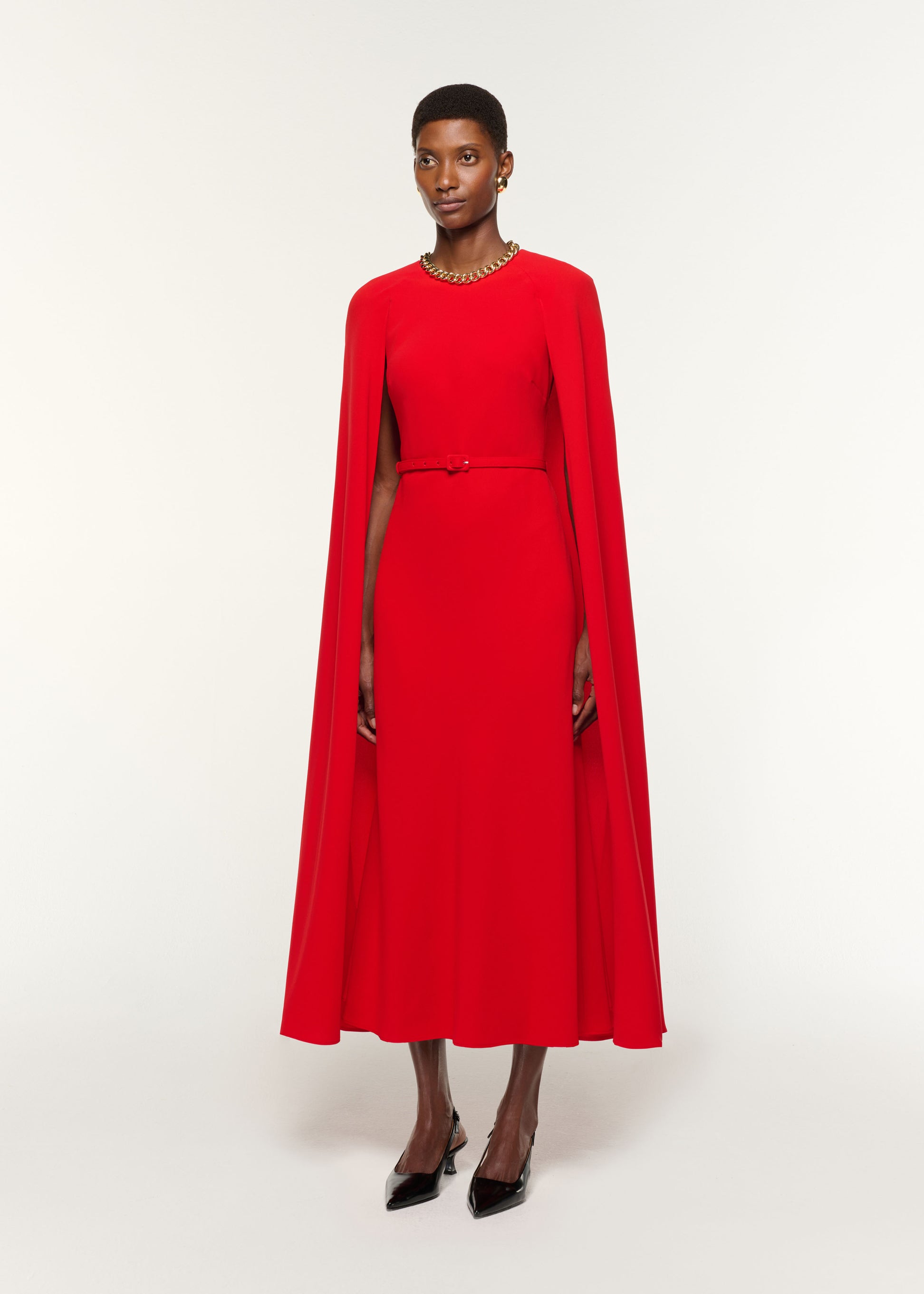 Side view of a model wearing the Light Cady Belted Cape Dress in Red