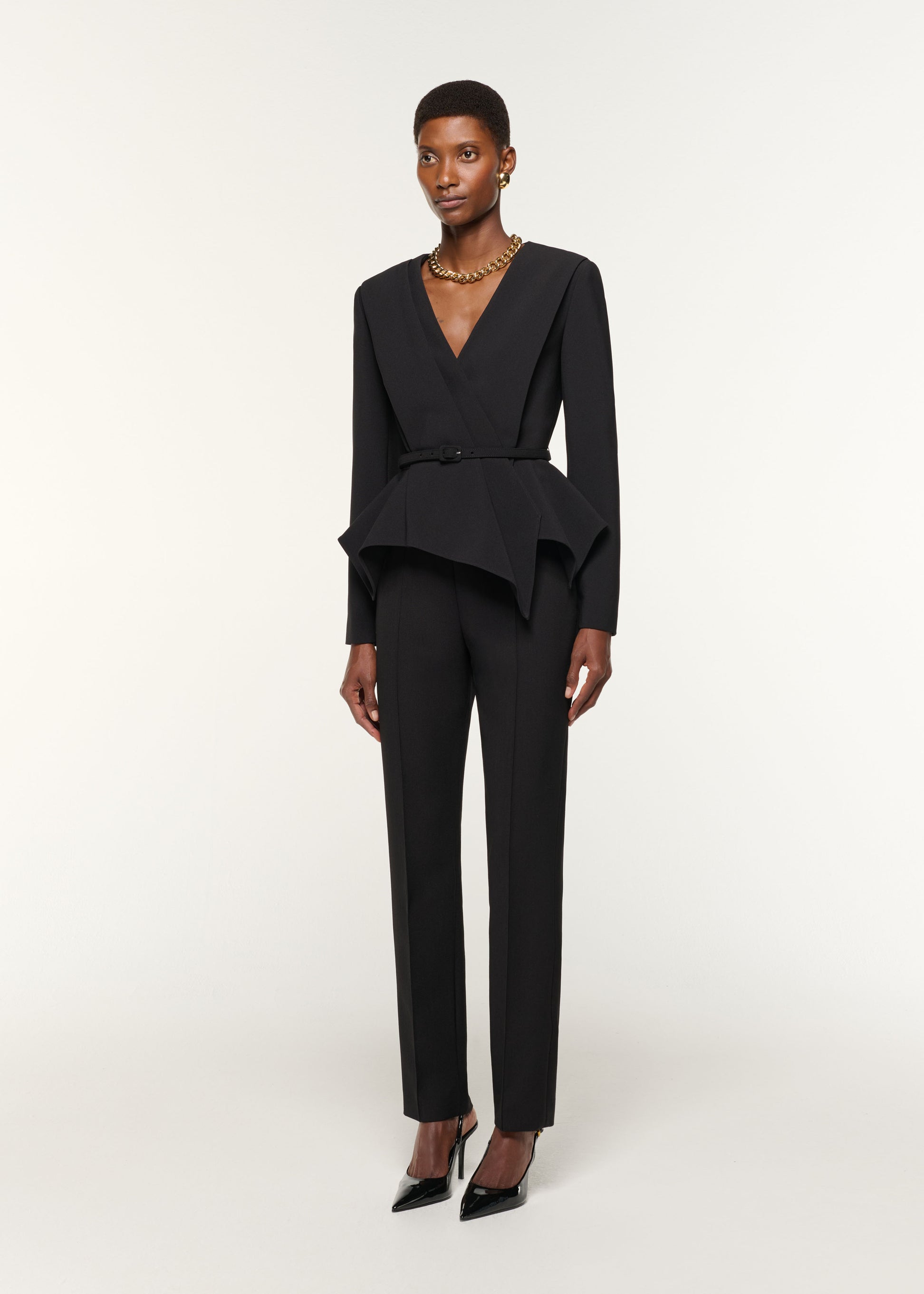 Side view of a model wearing the Asymmetrical Drape Peplum Crepe Jacket in Black