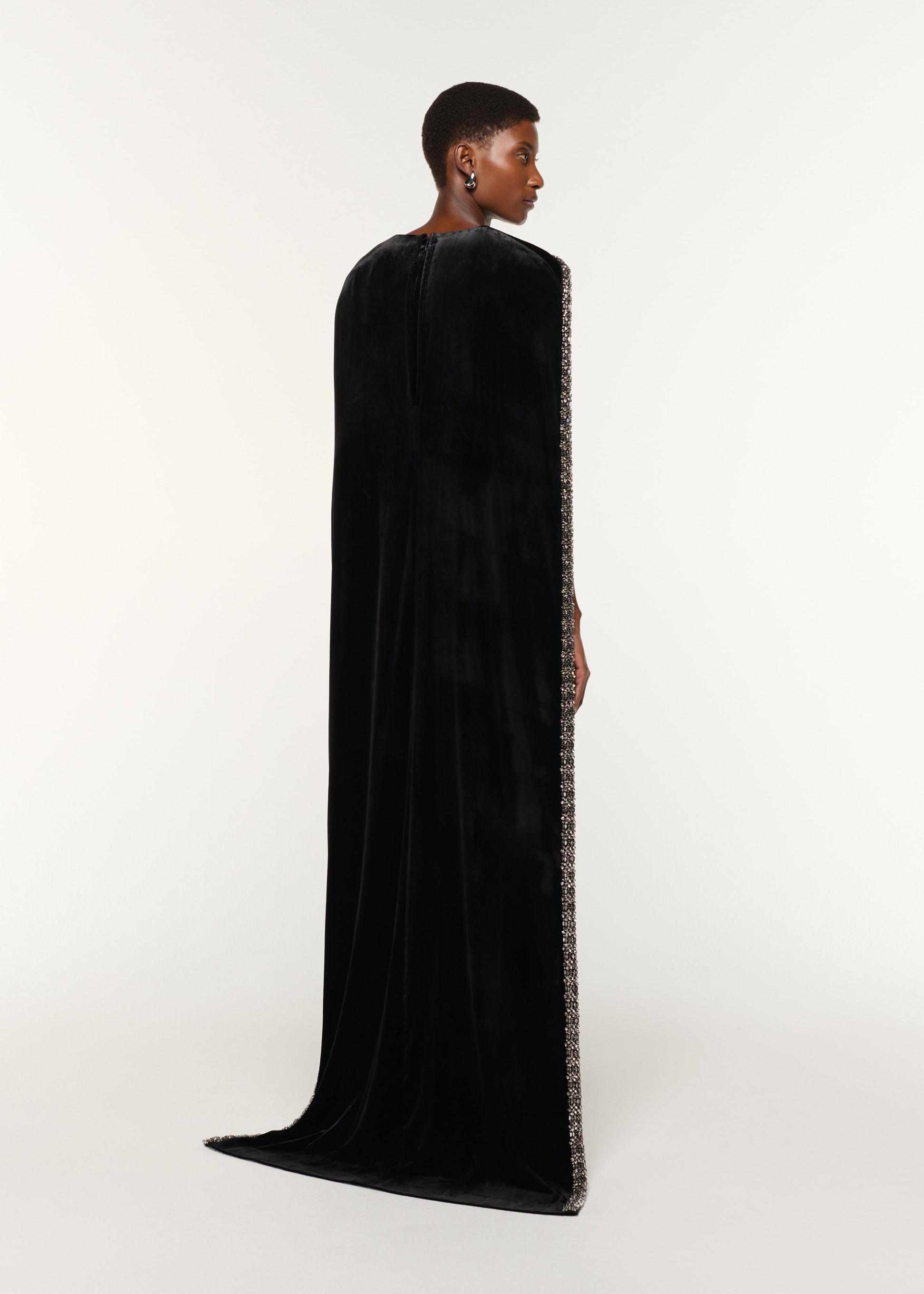 Back view of a model wearing the Embellished Cape Velvet Gown in Black