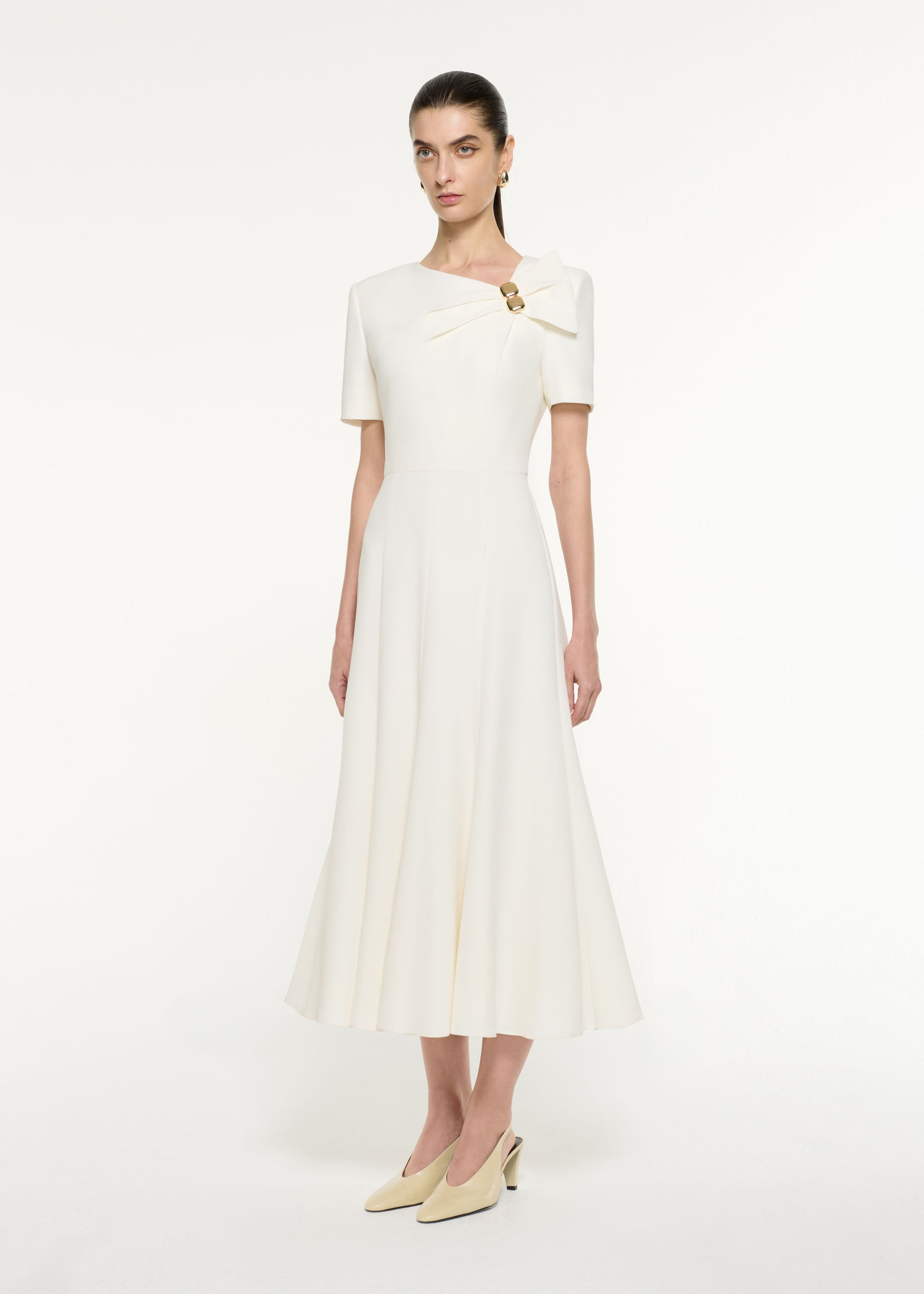 Side view of a model wearing the Bow Drape Light Cady Midi Dress in Cream