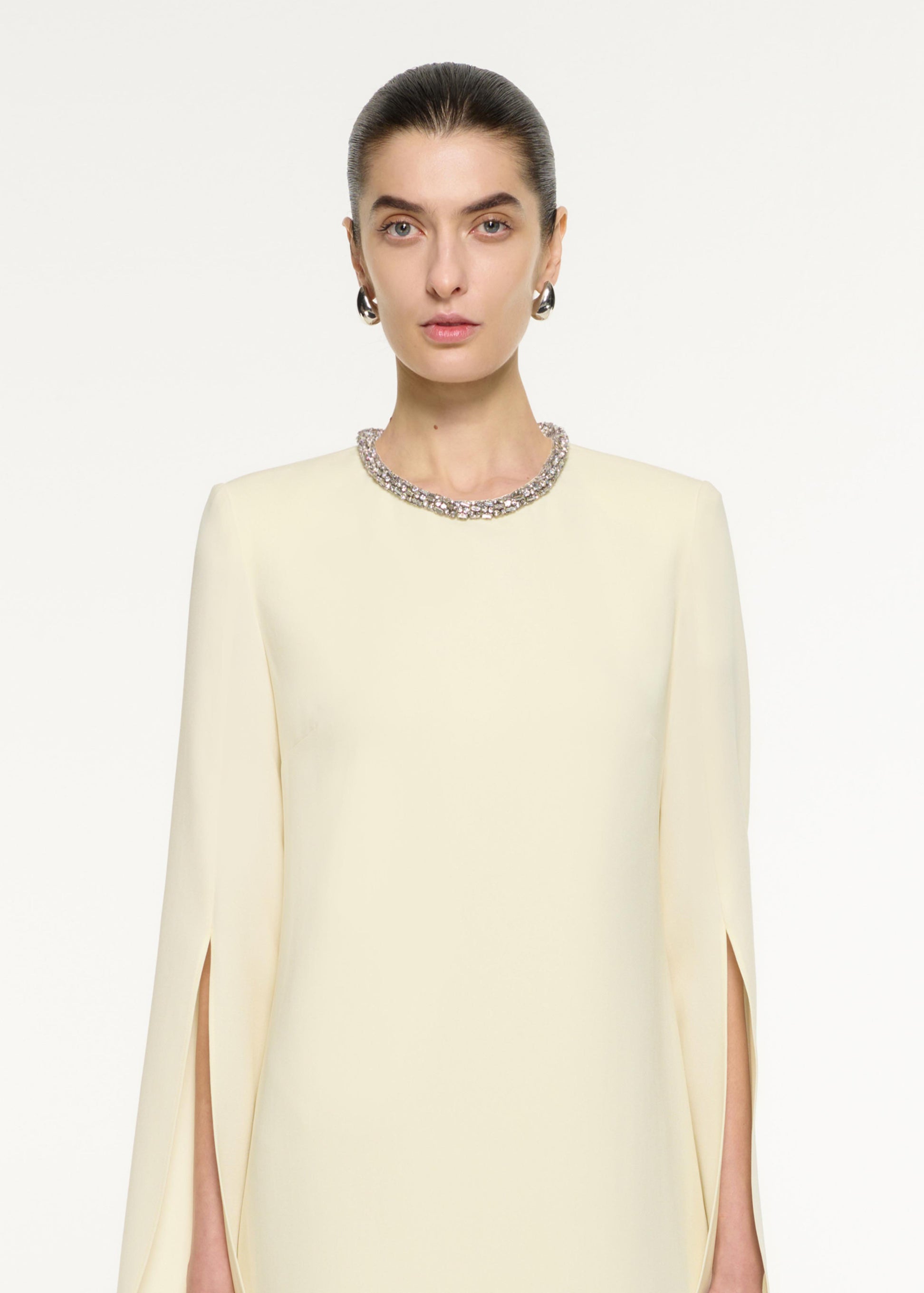 Close up of a model wearing the Cape Sleeve Embellished Mini Dress in Light Yellow