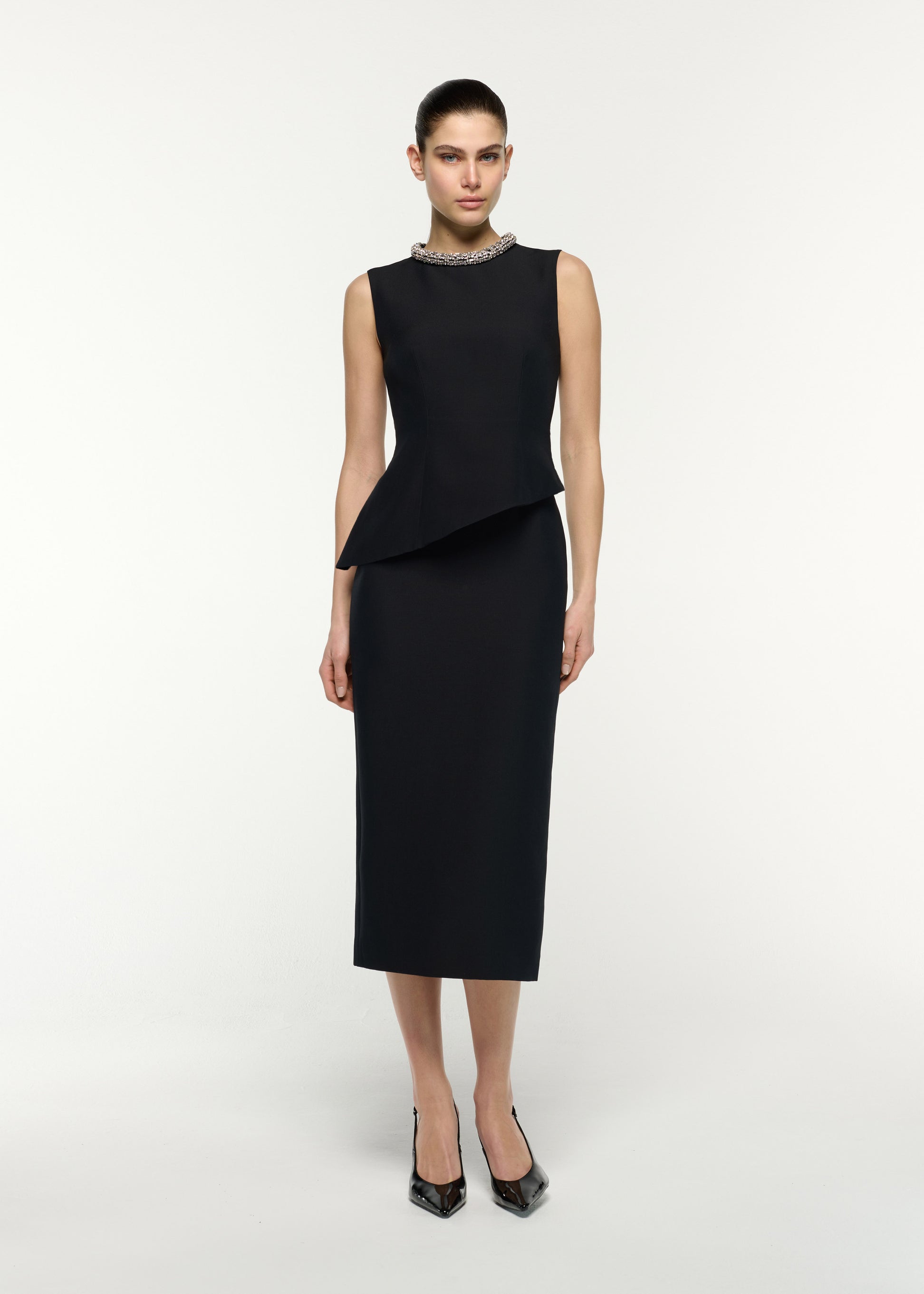 Front view of a model wearing the Crystal Neck Trimmed Asymmetric Peplum Midi Dress in Black
