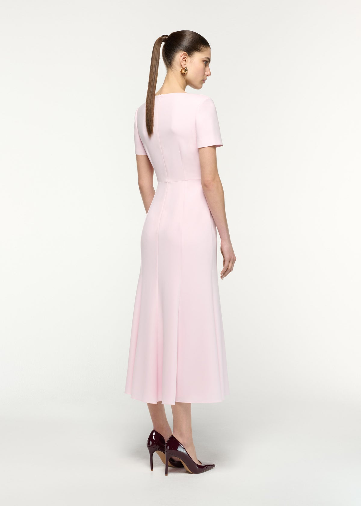 Back view of a model wearing the Short Sleeve Twist Drape Midi Dress in Pink