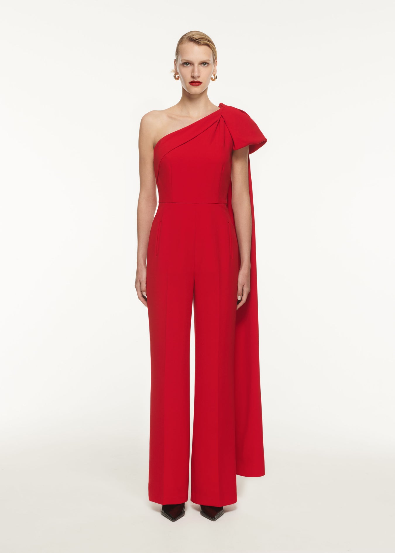 A woman wearing the Asymmetric Stretch Cady Jumpsuit in Red