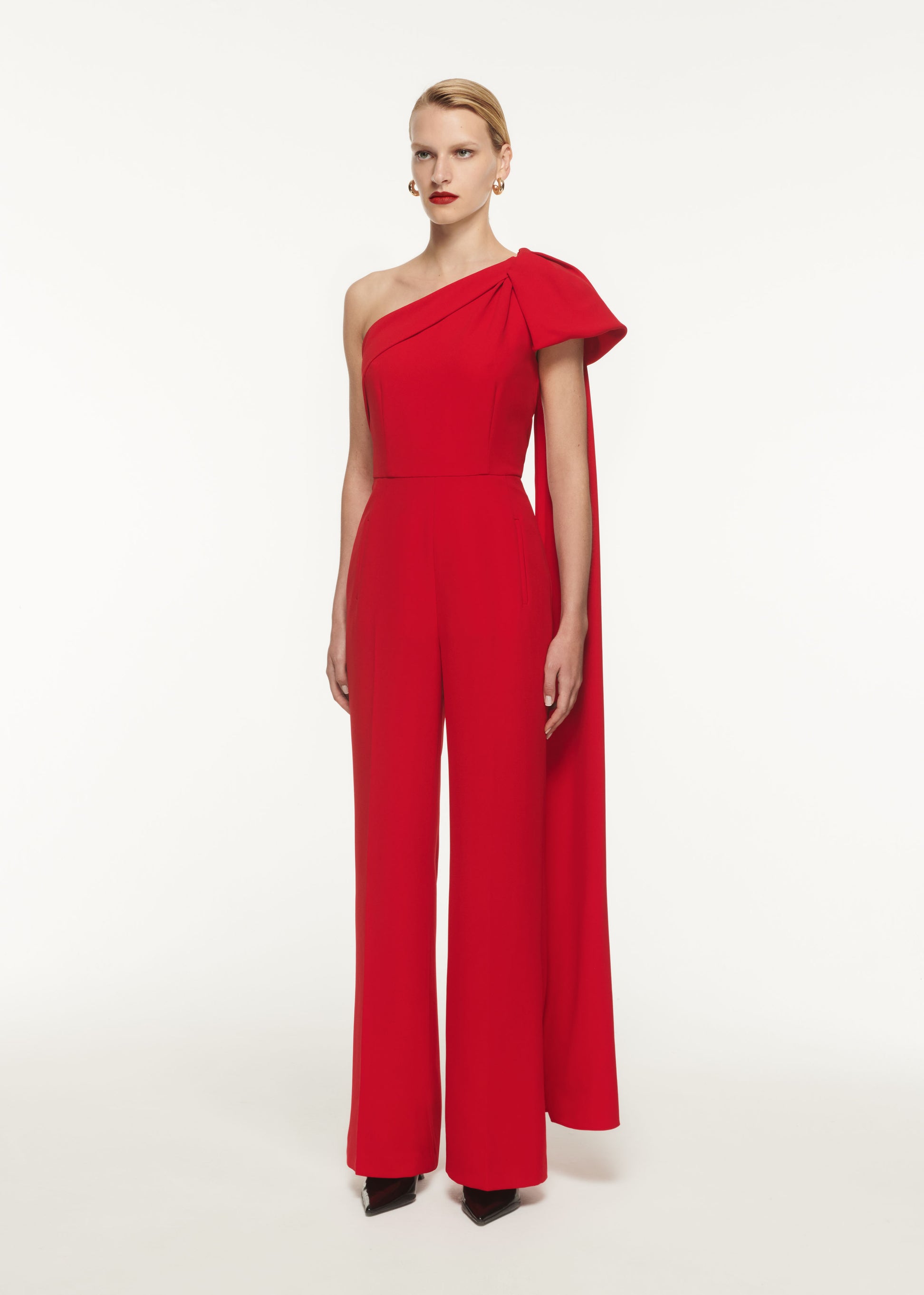 A woman wearing the Asymmetric Stretch Cady Jumpsuit in Red