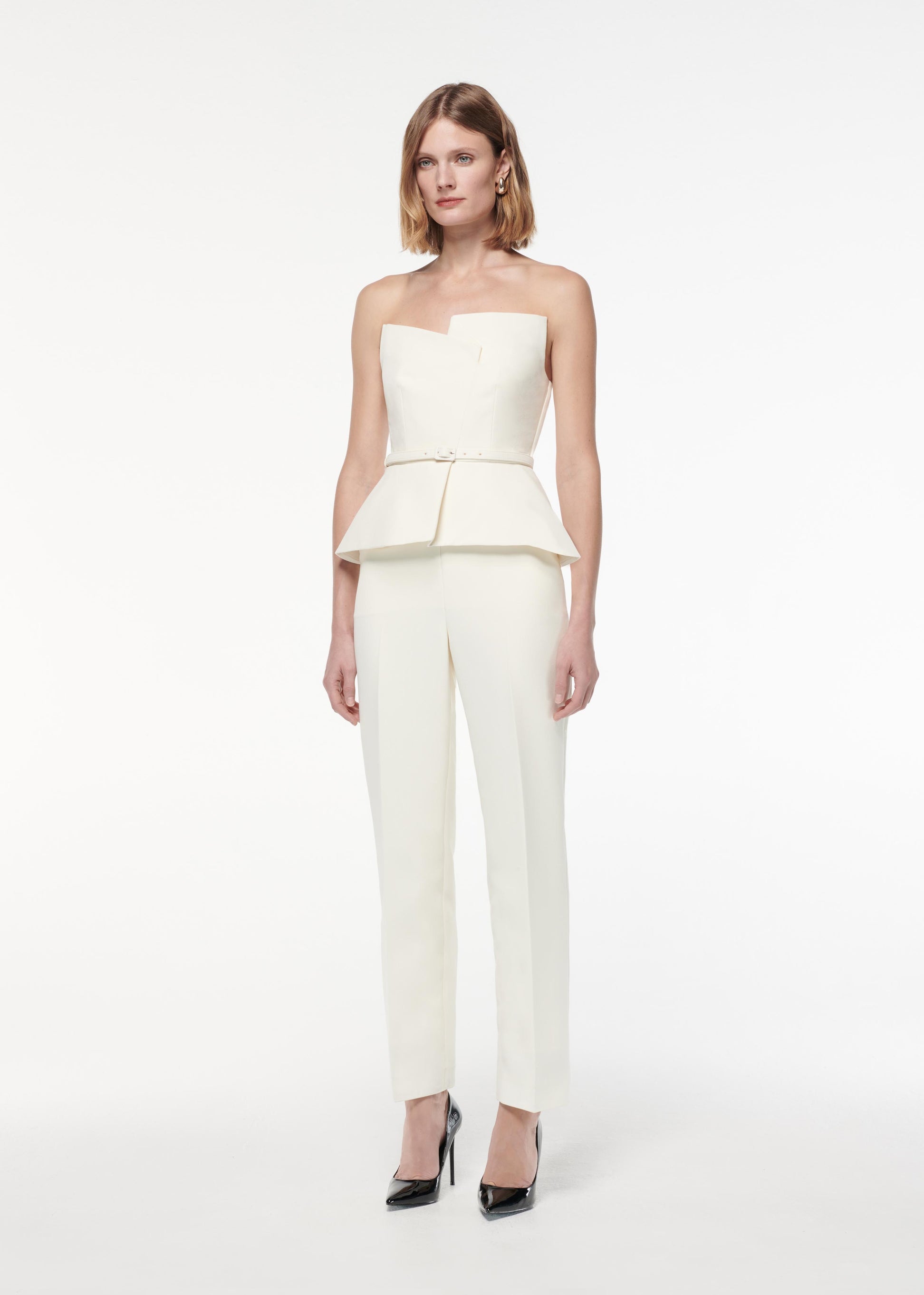 A photograph of a woman wearing a Strapless Peplum Crepe Jumpsuit in Cream