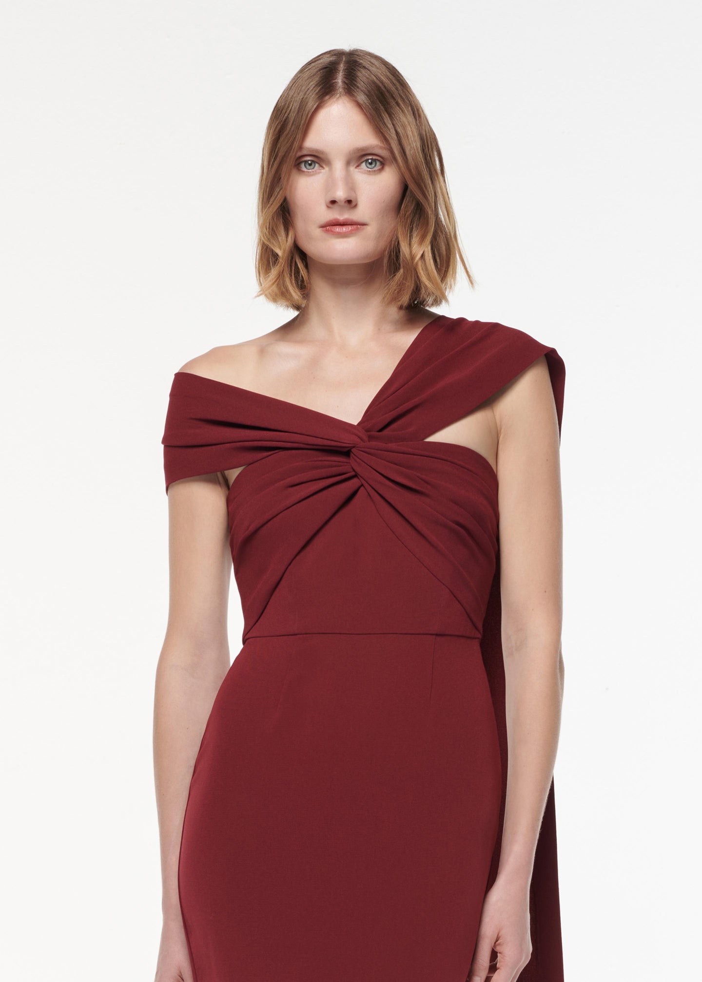 A photograph of a woman wearing a Asymmetric Light Cady Gown in Burgundy