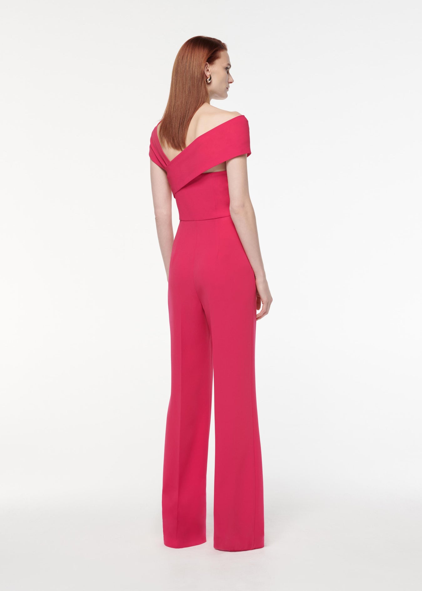 A photograph of a woman wearing a Asymmetric Light Cady Jumpsuit in Pink