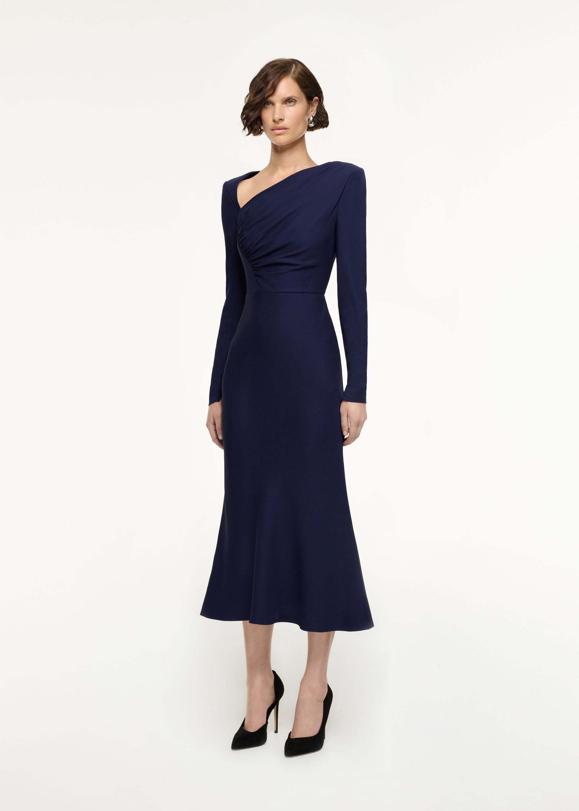 Side view of a model wearing the Asymmetric Drape Stretch Cady Midi Dress in Navy