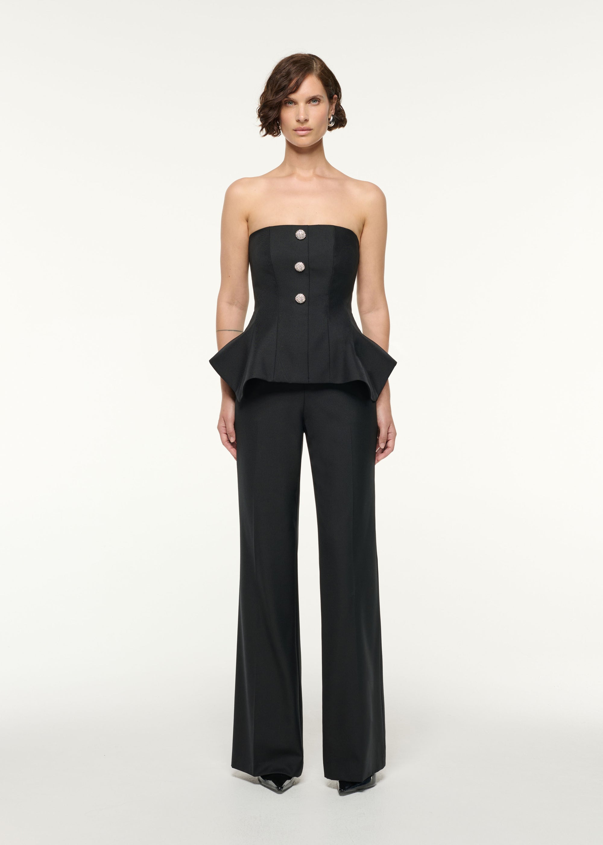 Front view of a model wearing the Crystal Button Peplum Wool Jumpsuit in Black