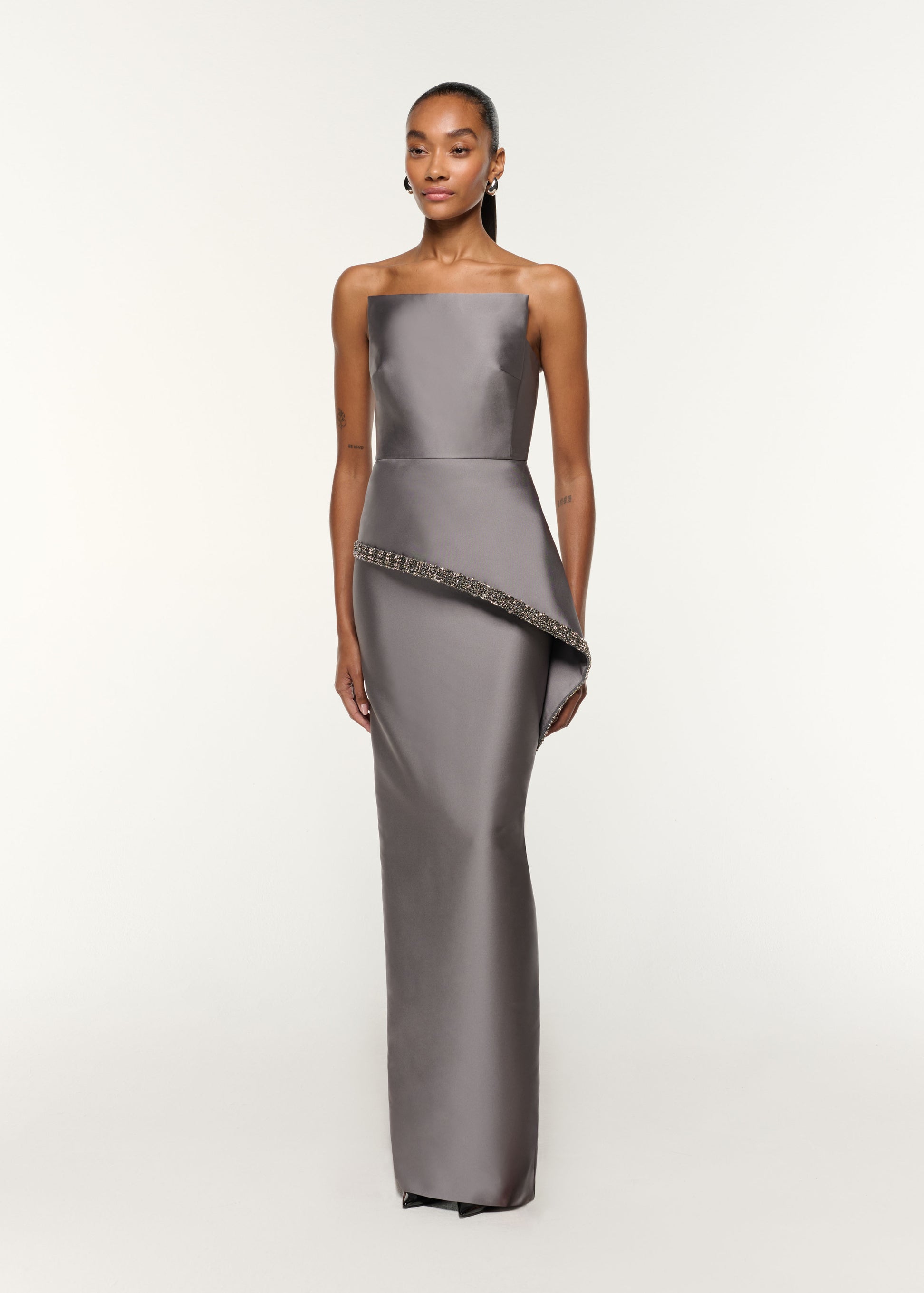 Side view of a model wearing the Square Neck With Crystal Trim Peplum Taffeta Gown in Grey