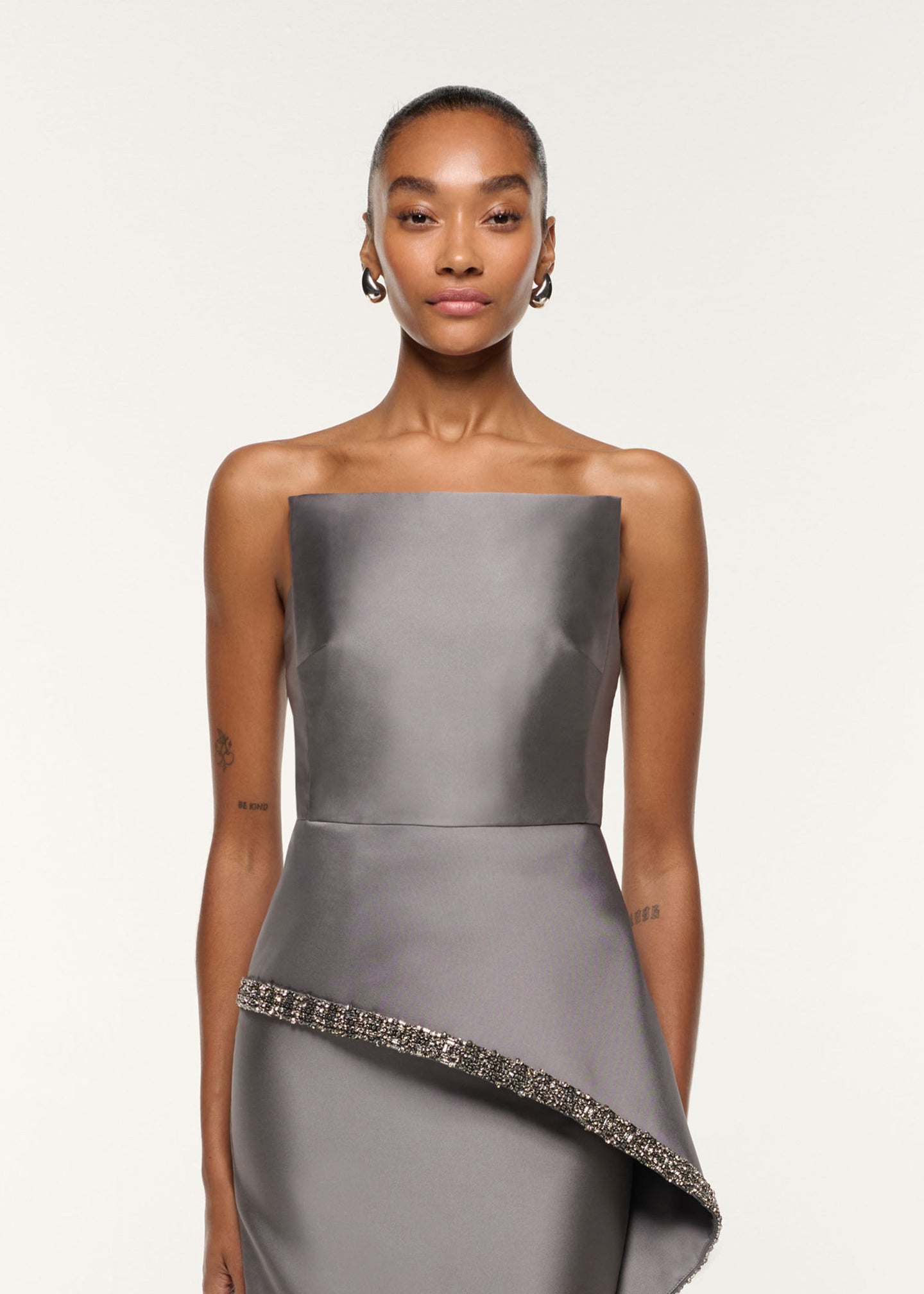 Close up of a model wearing the Square Neck With Crystal Trim Peplum Taffeta Gown in Grey