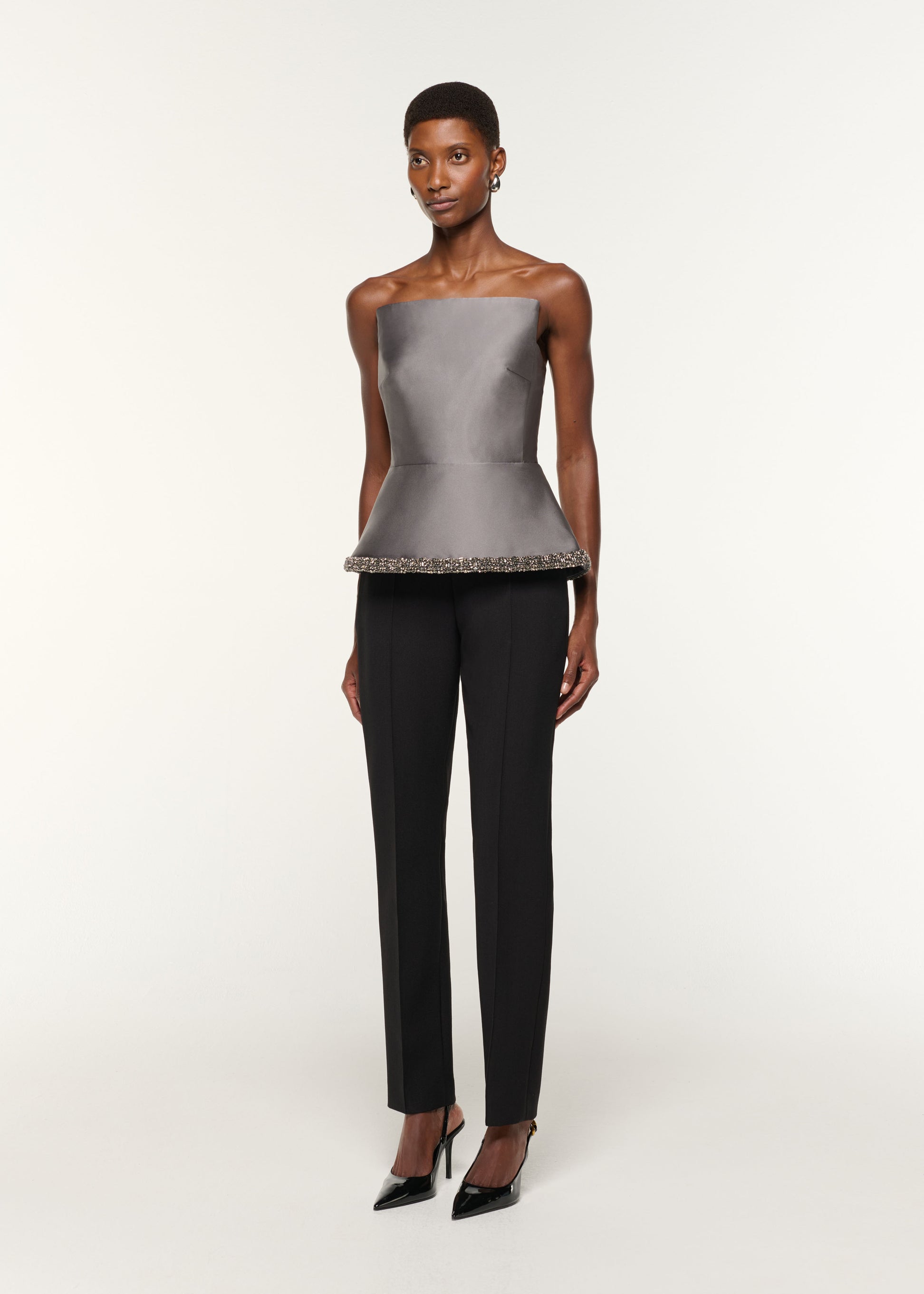 Side view of a model wearing the Square Neck With Crystal Trim Peplum Taffeta Top in Grey