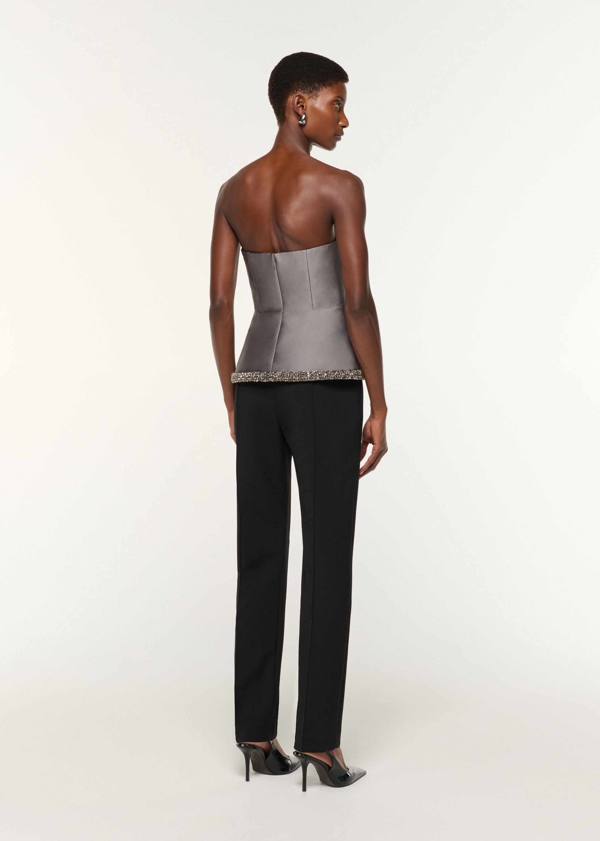 Back view of a model wearing the Square Neck With Crystal Trim Peplum Taffeta Top in Grey