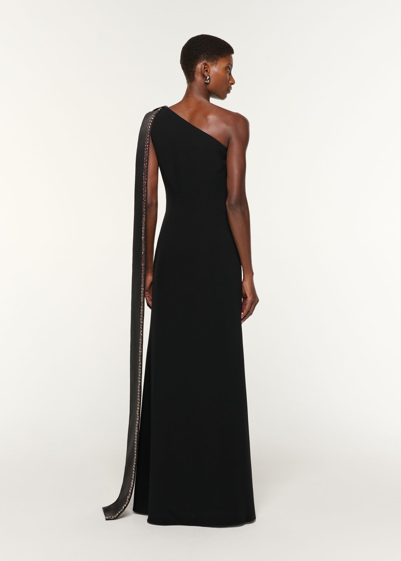 Back view of a model wearing the Contrast Crystal Trimmed Bow Satin Crepe Gown in Black