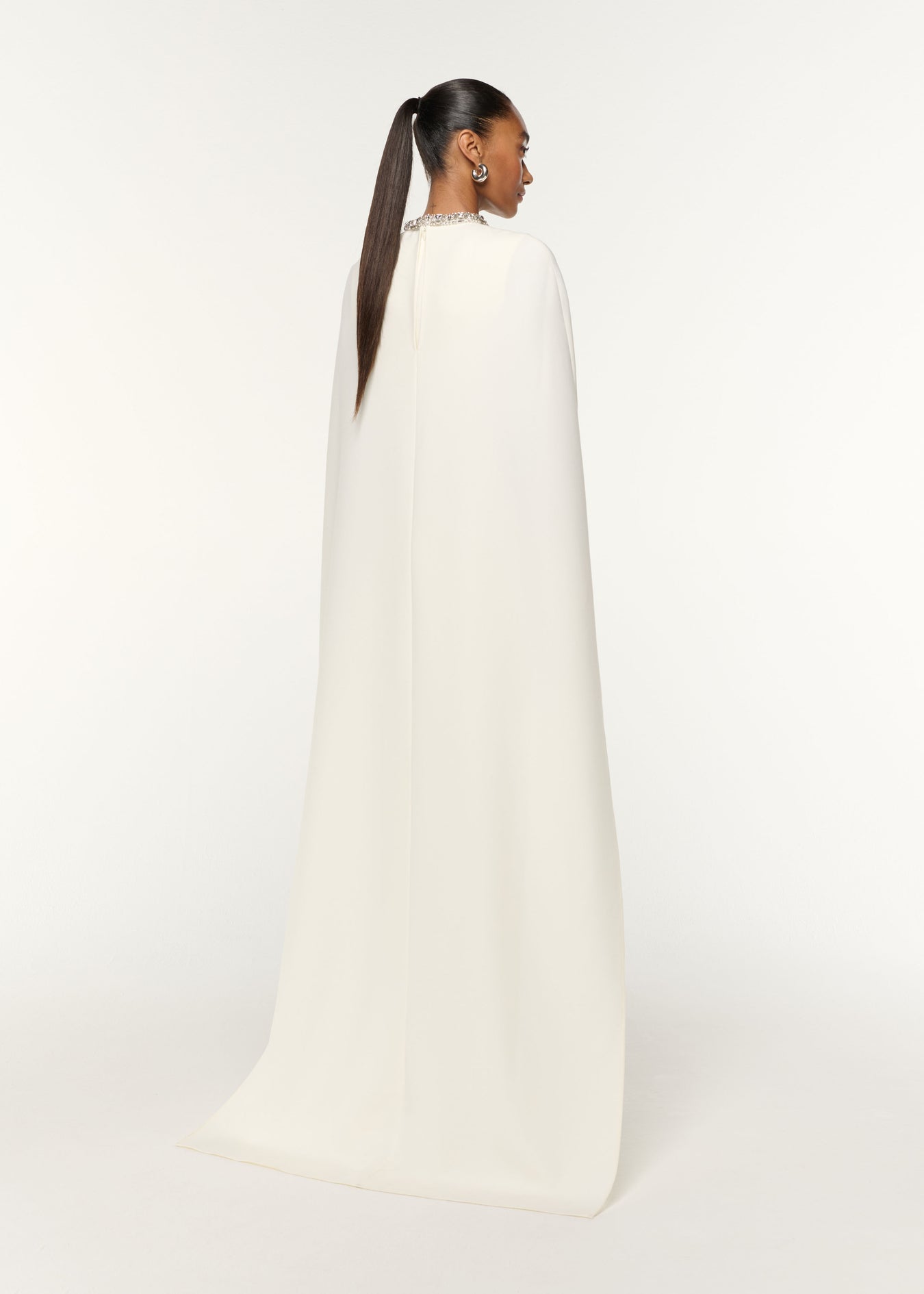 Back view of a model wearing the Crystal Neckline Crepe Cape Gown in Cream