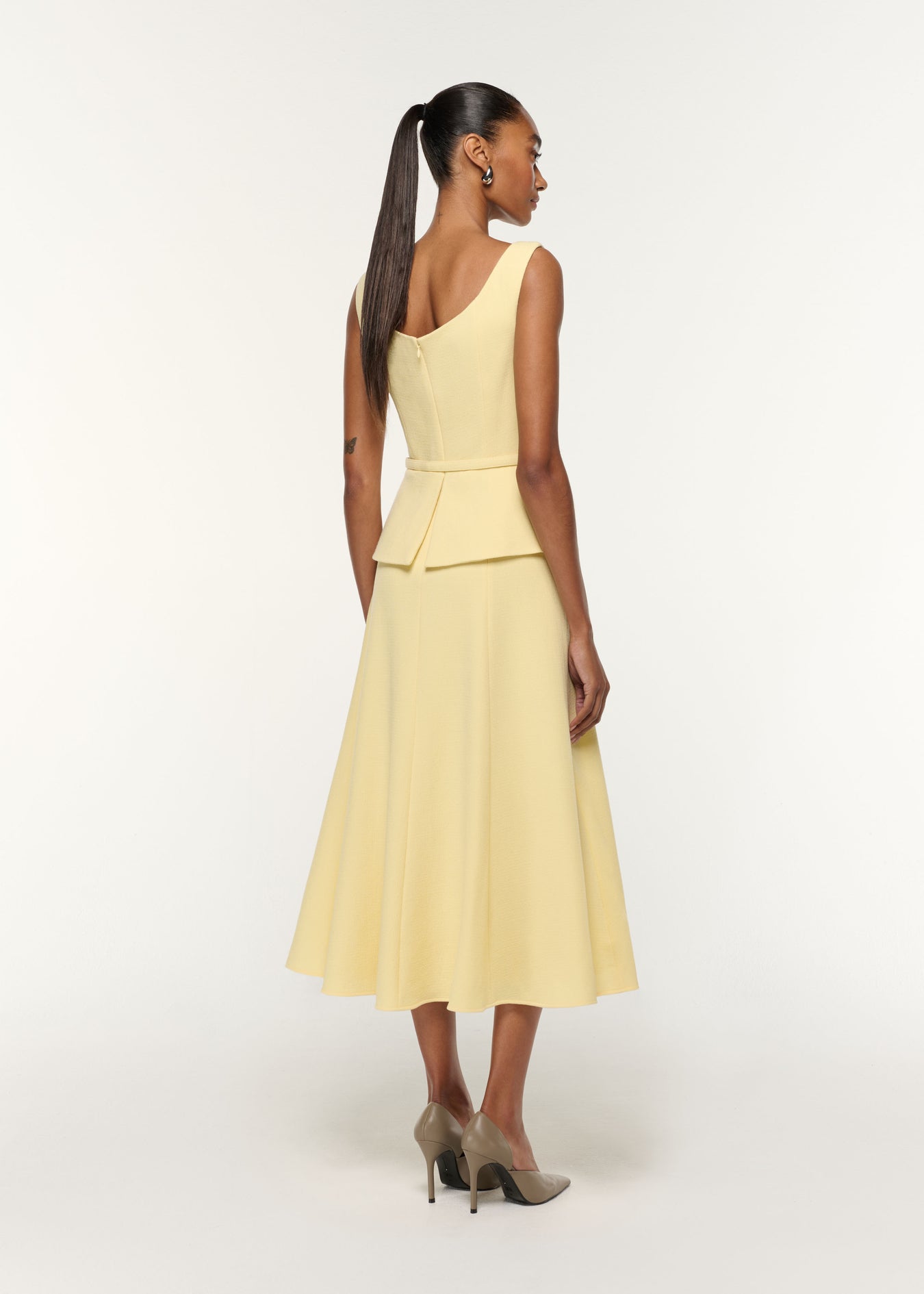 Back view of a model wearing the Structured Peplum Wool Crepe Dress in Yellow